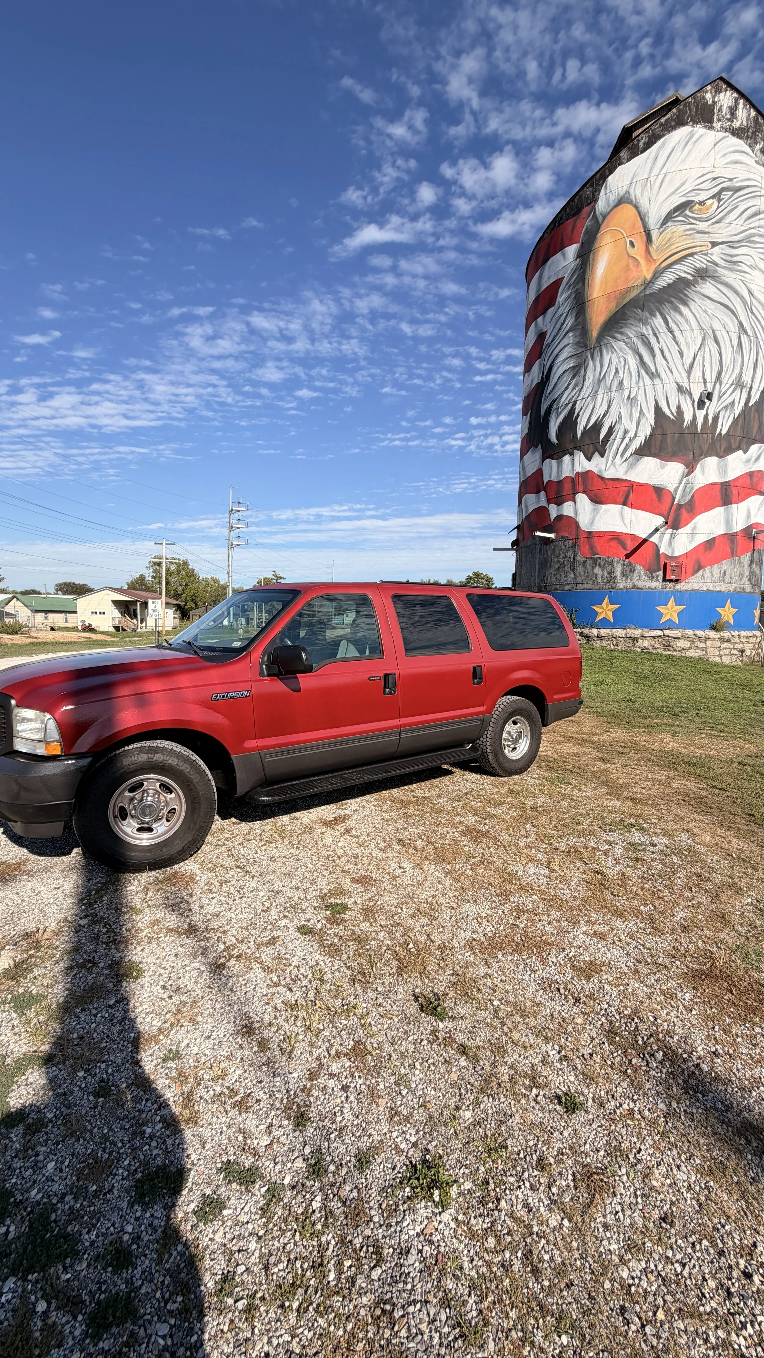 Red SUV parked on gravel with a large mural of an eagle painted on a silo in the background.