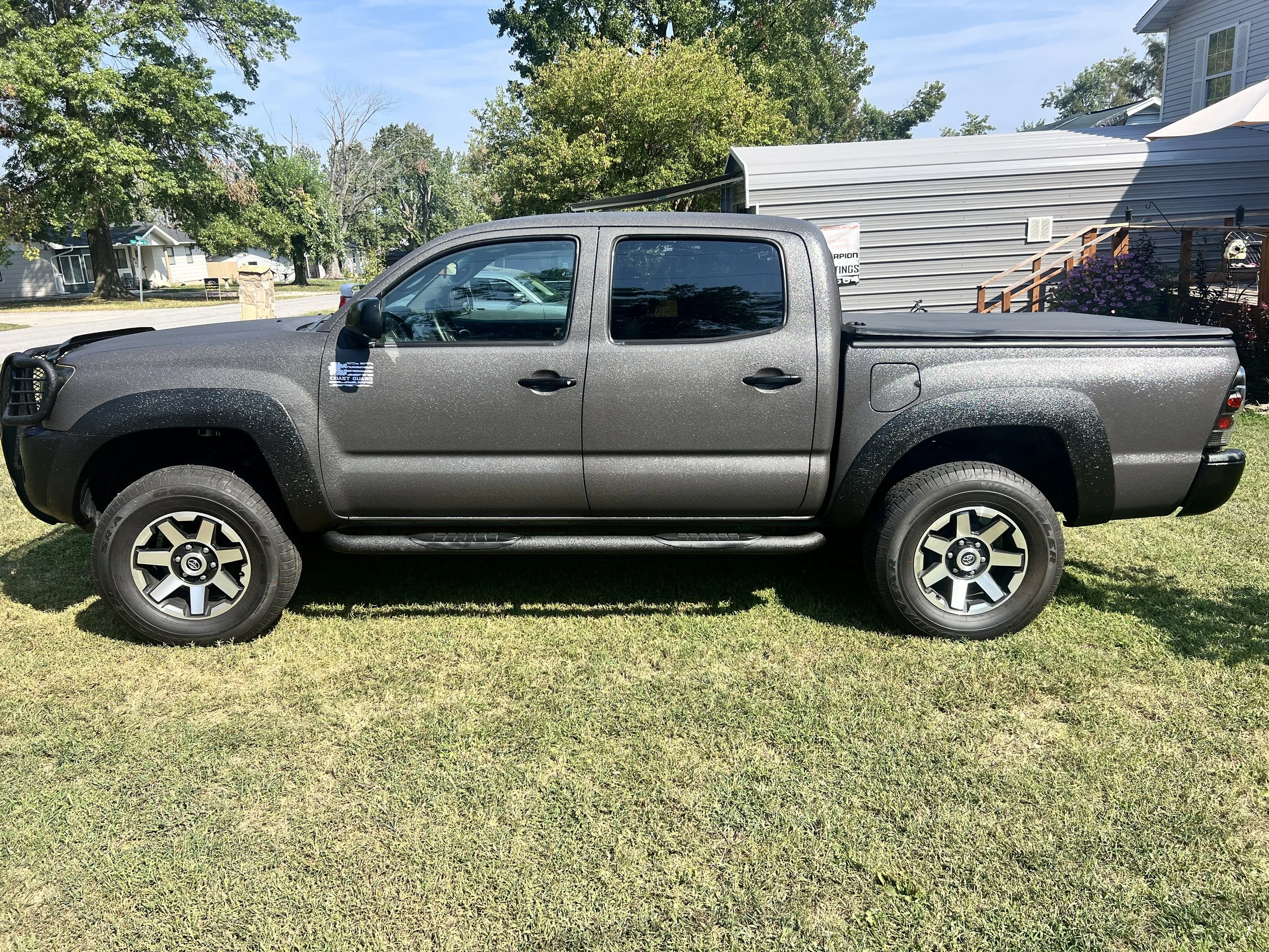 Gray pickup truck parked on grass in a suburban neighborhood with trees, houses, and a camper trailer in the background.