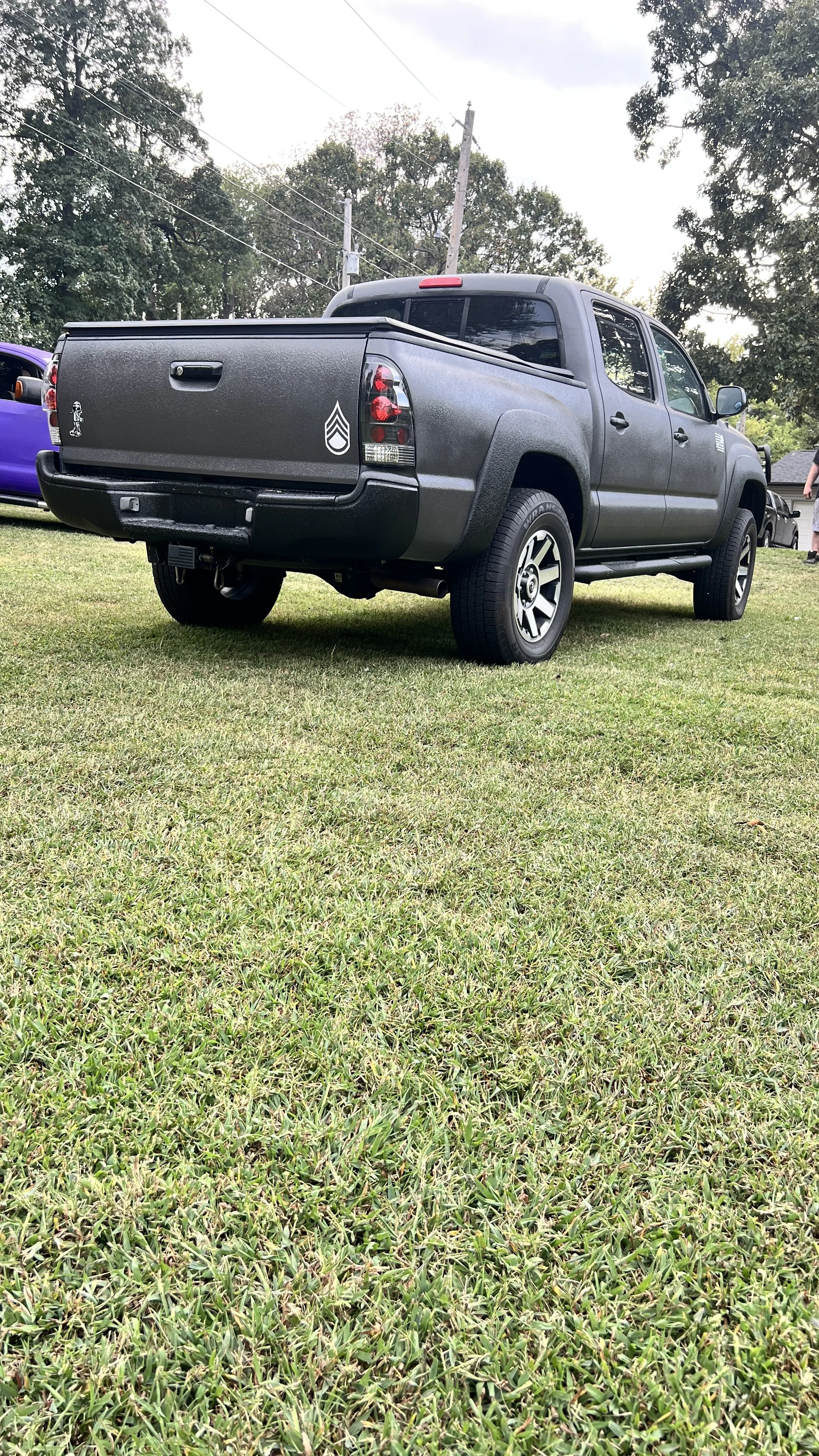 A gray pickup truck parked on green grass with trees and power lines in the background.