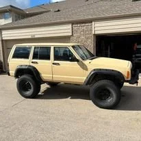 Beige Jeep SUV with large off-road tires parked outside a garage.