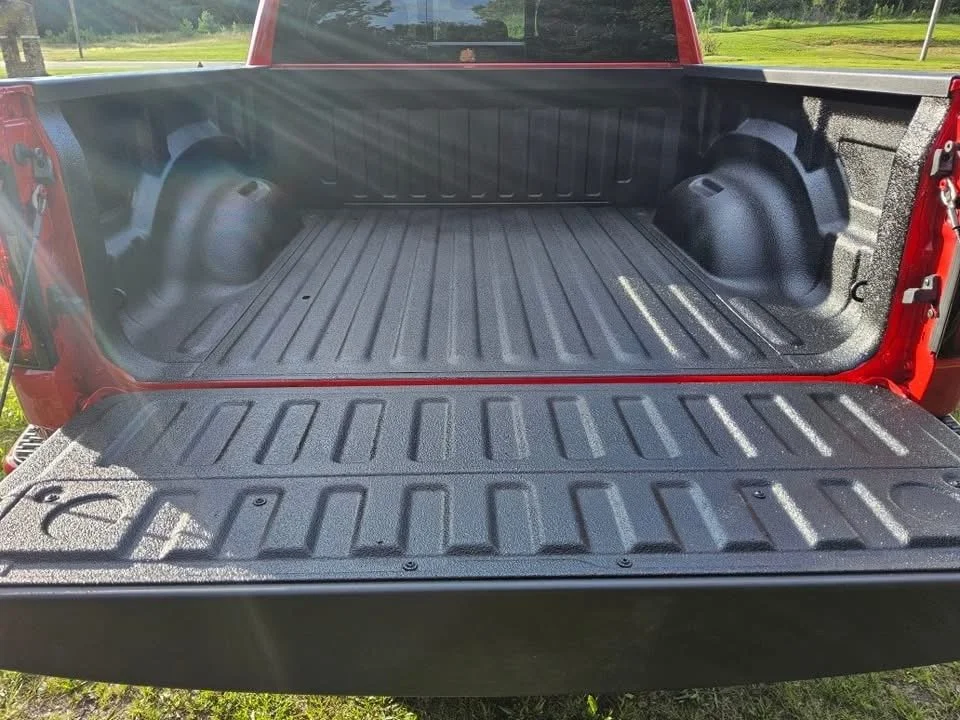 The open bed of a red pickup truck showing a clean, black plastic truck bed liner with wheel well covers.