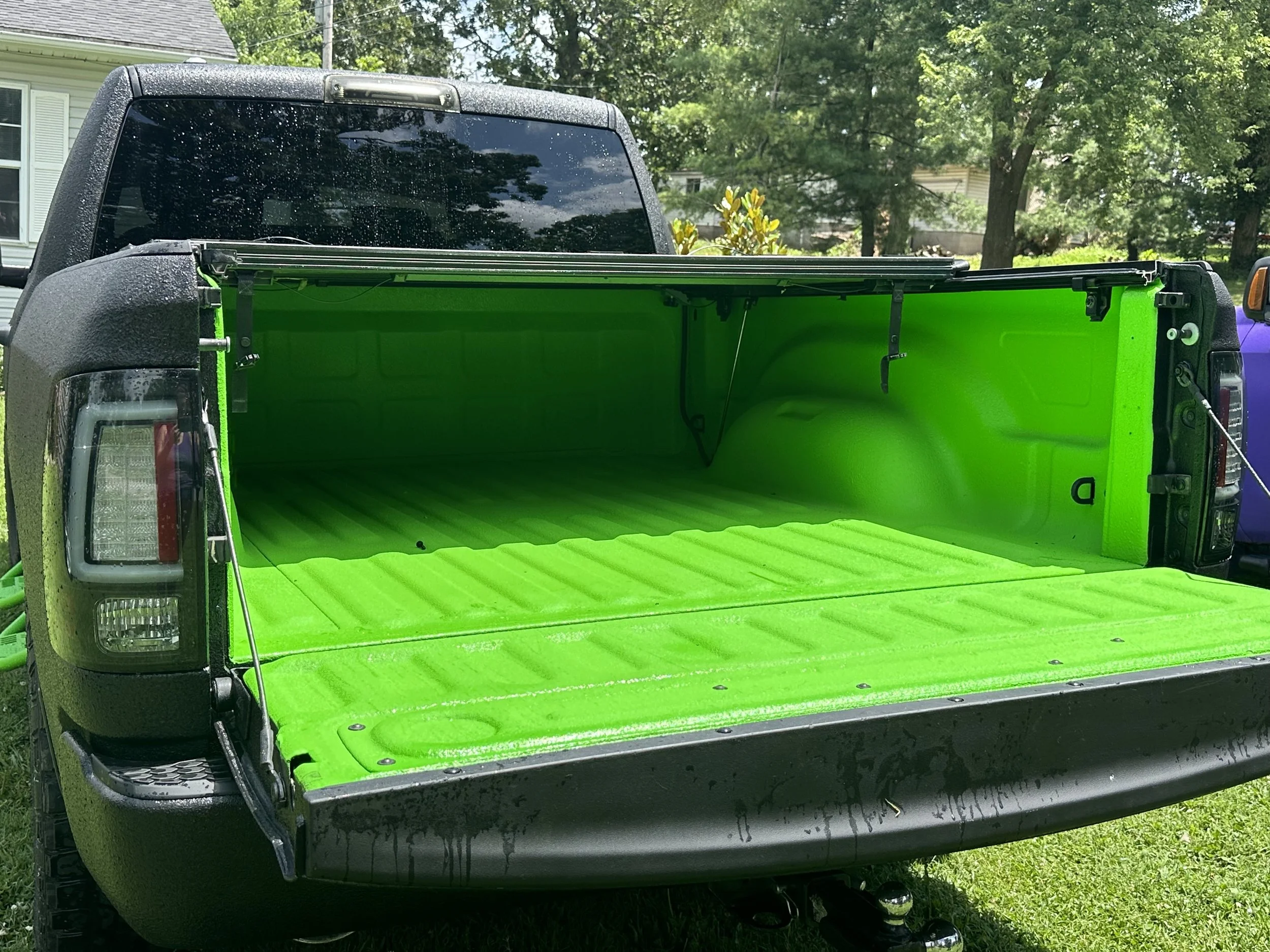 Open truck bed with bright green lining on a grassy yard, with trees and houses in the background.