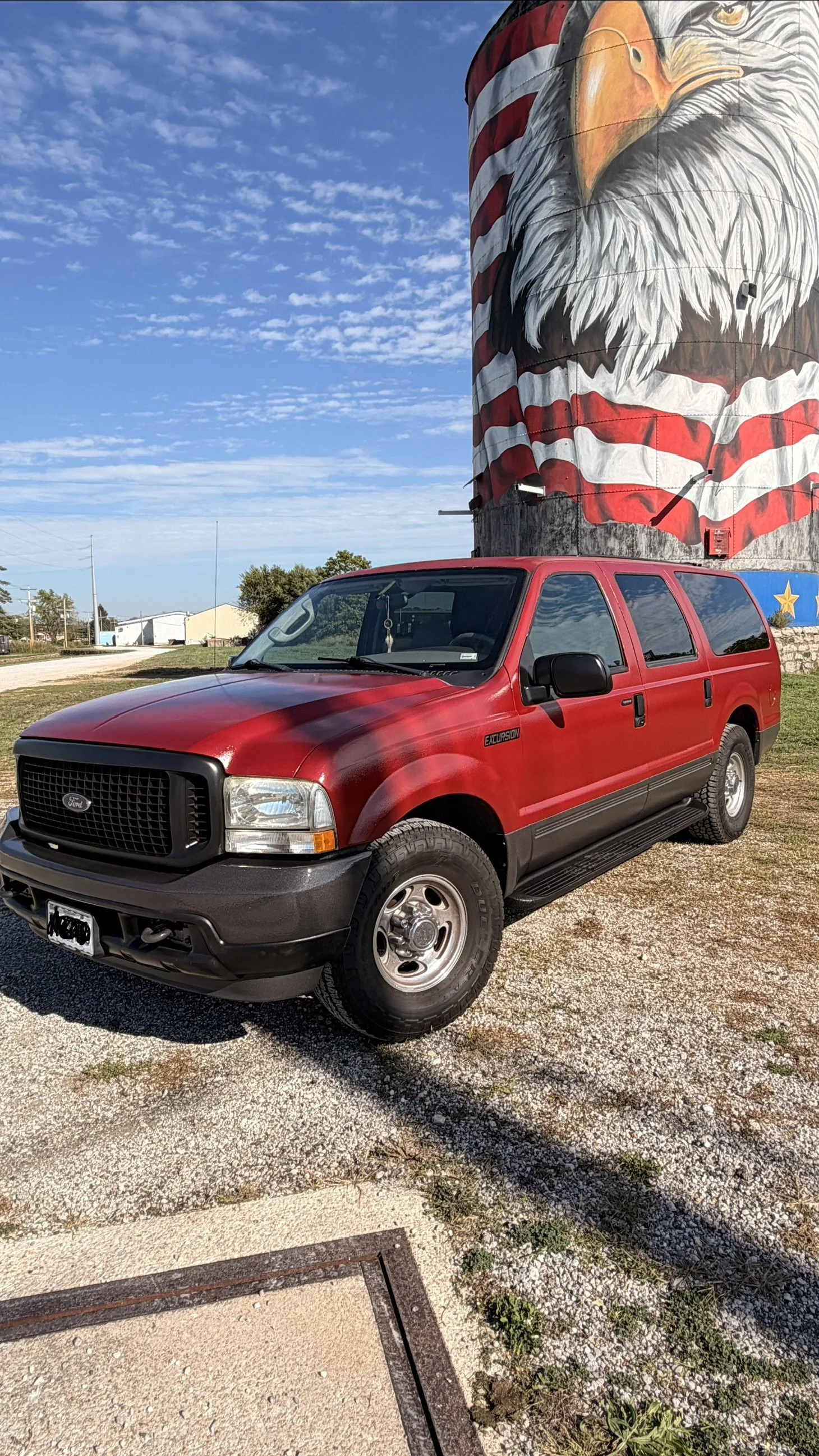 Red Ford Excursion parked outdoors with a large painted eagle mural on a silo in the background