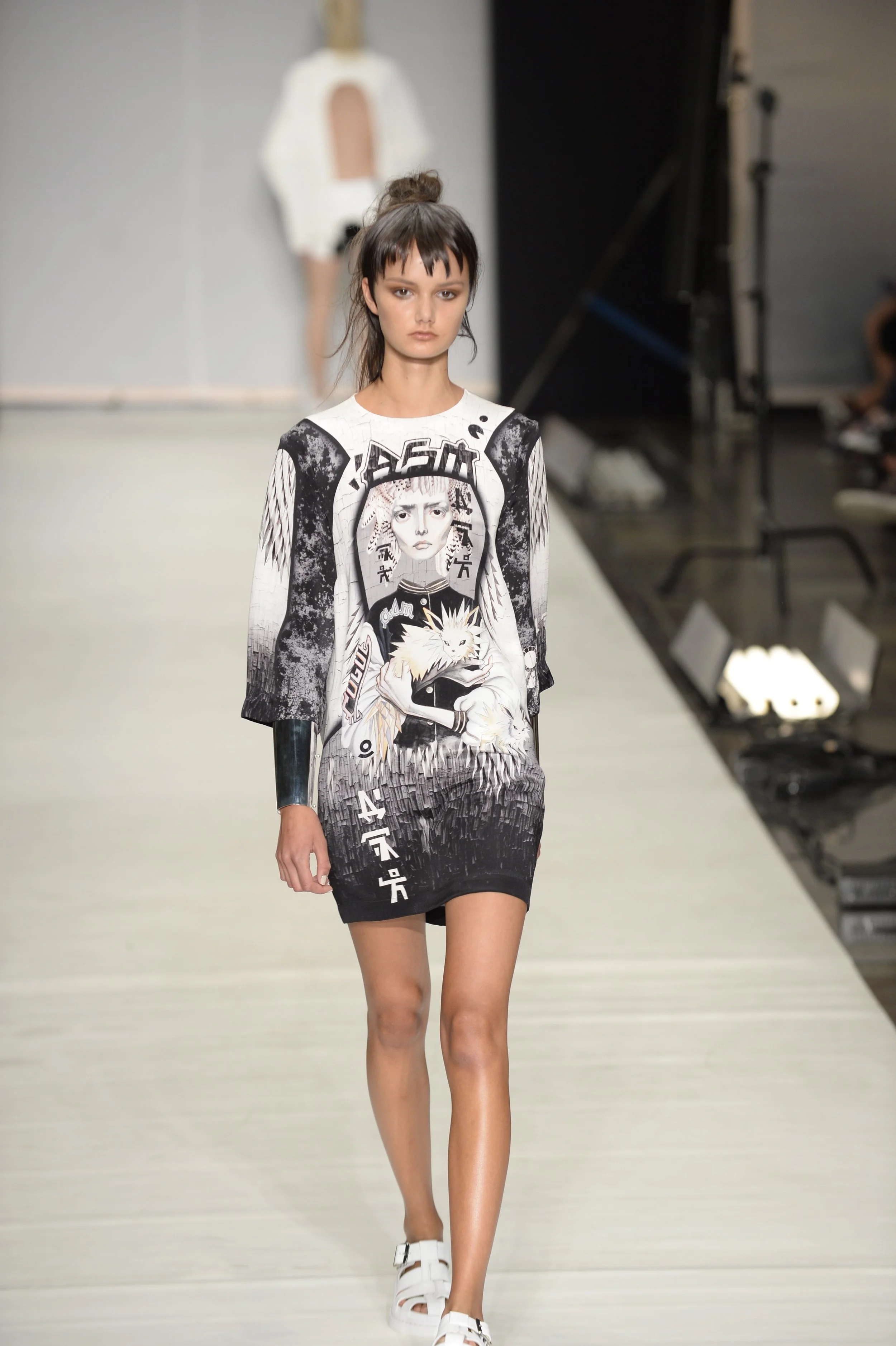 A fashion model walking on the runway during a fashion show, wearing a graphic black-and-white dress featuring anime-style artwork.