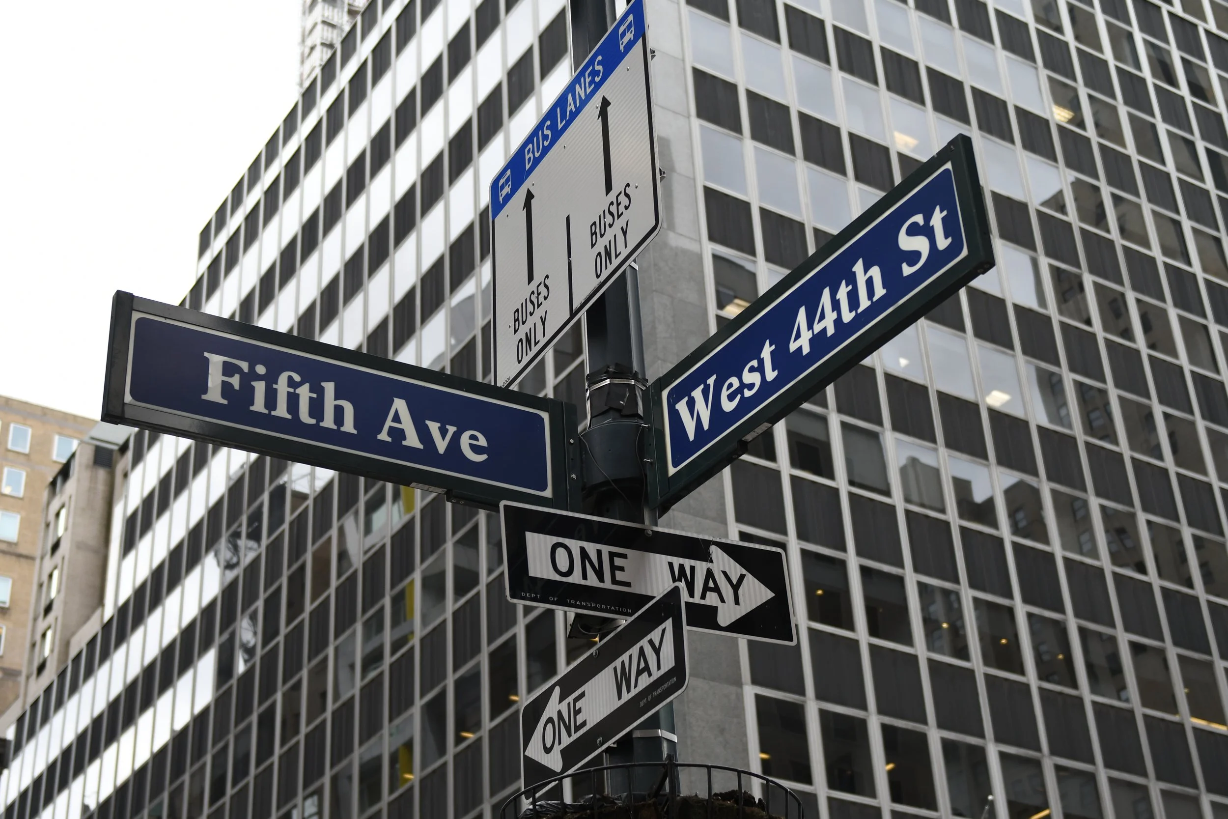 Street signs at the corner of Fifth Avenue and West 44th Street in New York City, with buildings in the background.