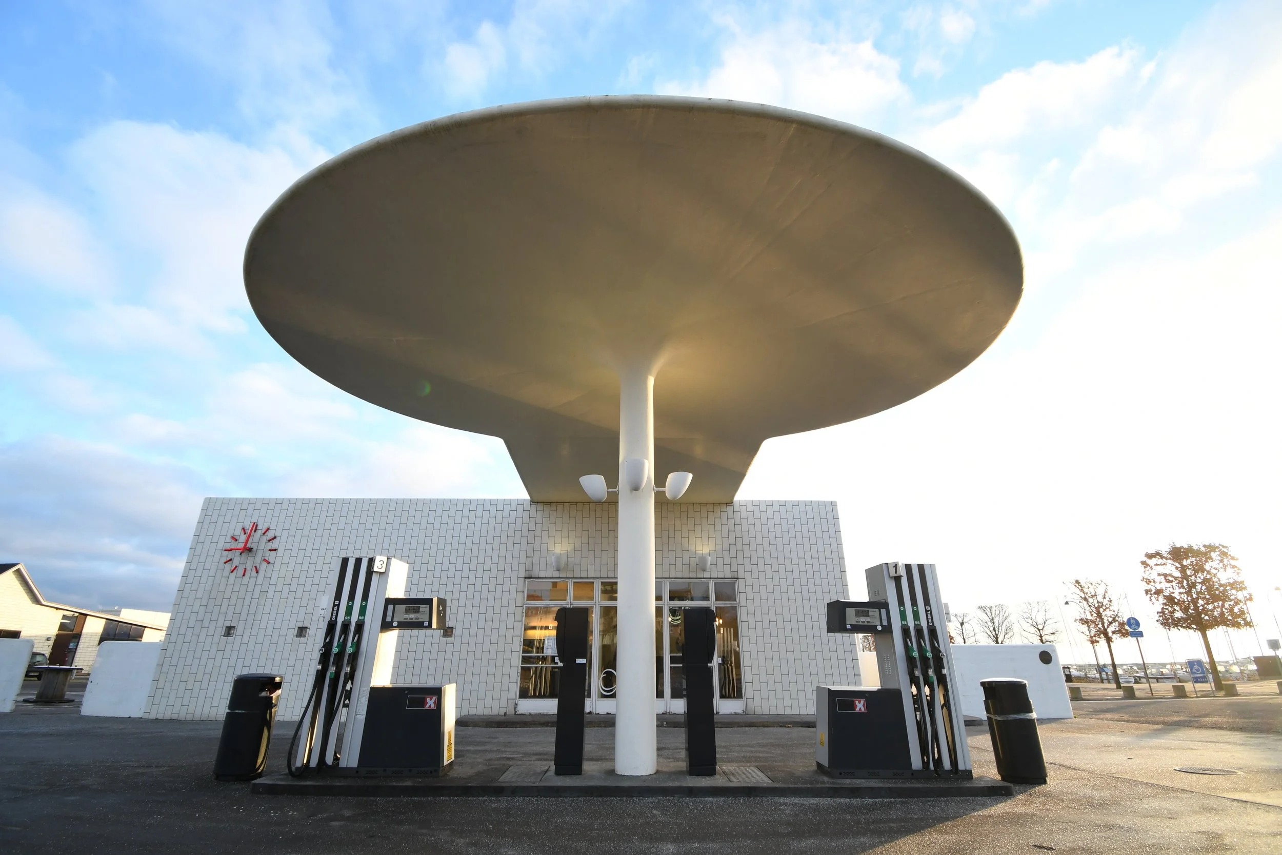 Unique gas station with a large disc-shaped canopy, modern white brick building, and multiple fuel pumps outdoors.