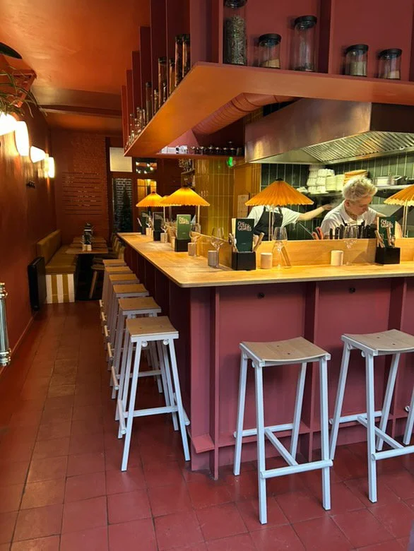 Intérieur d'un restaurant ou bar avec des décorations en céramique jaune, un miroir rond, des lampes murales, et des tables avec des verres à vin et des bougies.