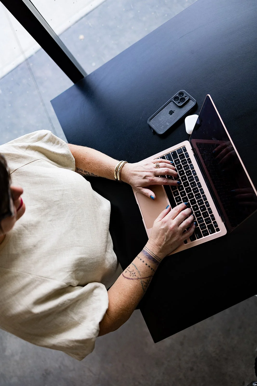 Person using a pink laptop at a black table, with an iPhone and AirPods nearby.