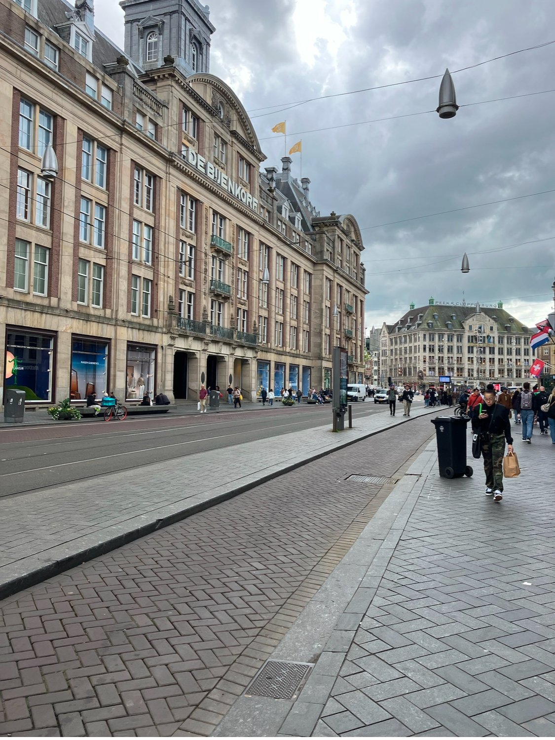 City street scene with historic building, tram tracks, pedestrians, and cloudy sky.