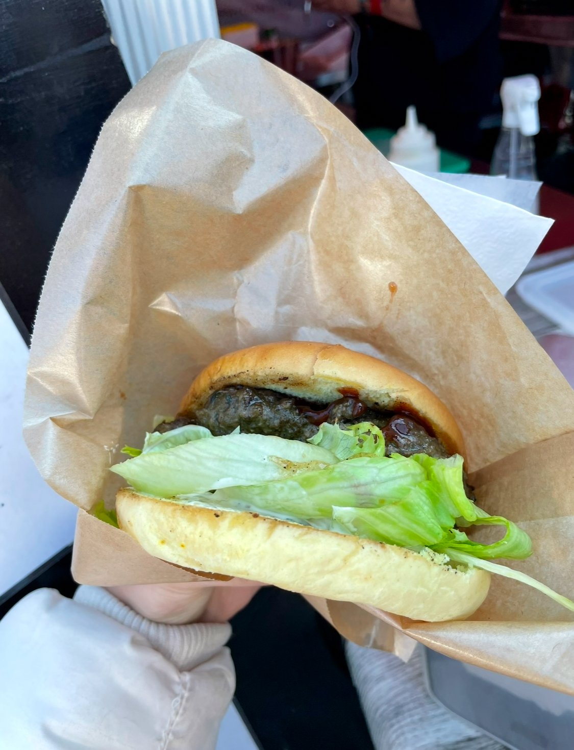 A burger wrapped in brown paper, with lettuce and a beef patty with barbecue sauce visible inside.