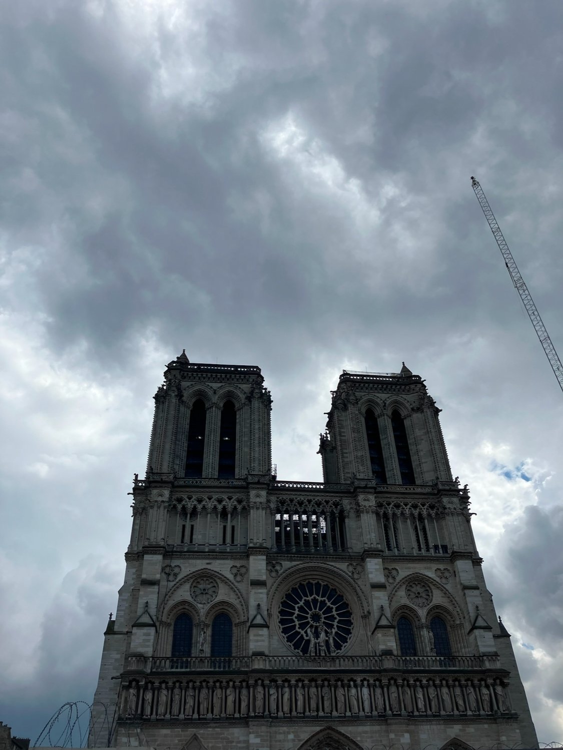 The Notre-Dame Cathedral in Paris with dark cloudy skies overhead, showing its Gothic architectural features and iconic twin towers.