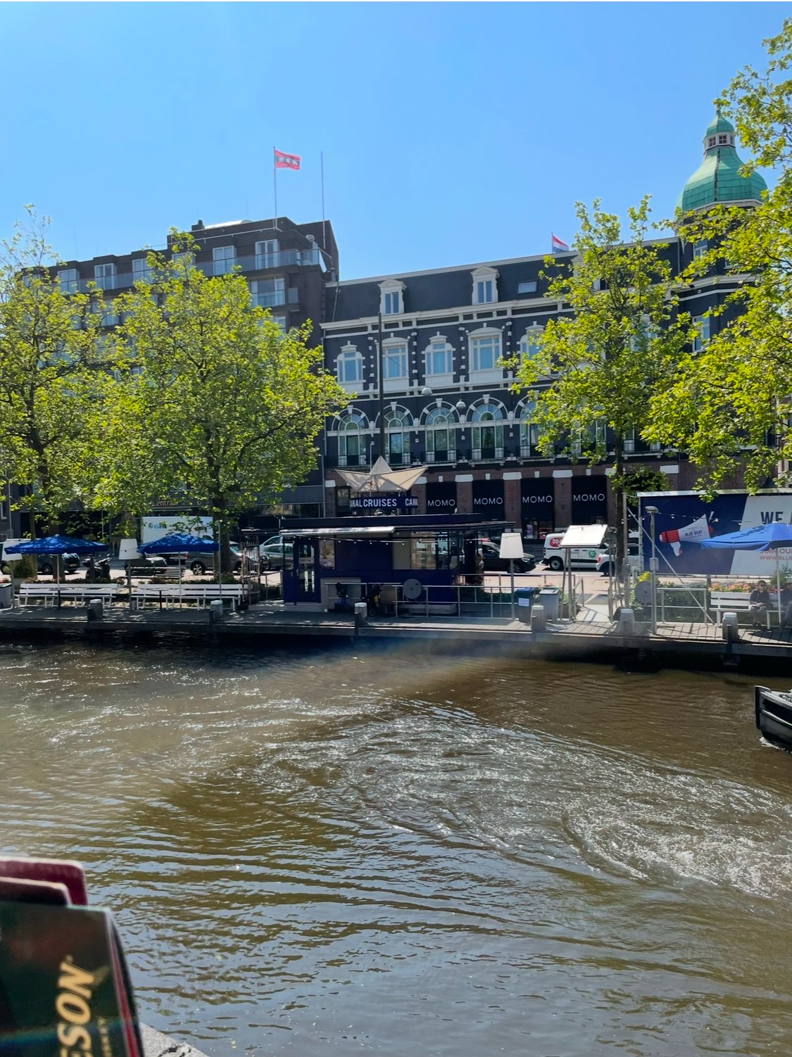 A view of a city waterfront with a building, trees, and a waterway, and a boat docked at the pier.