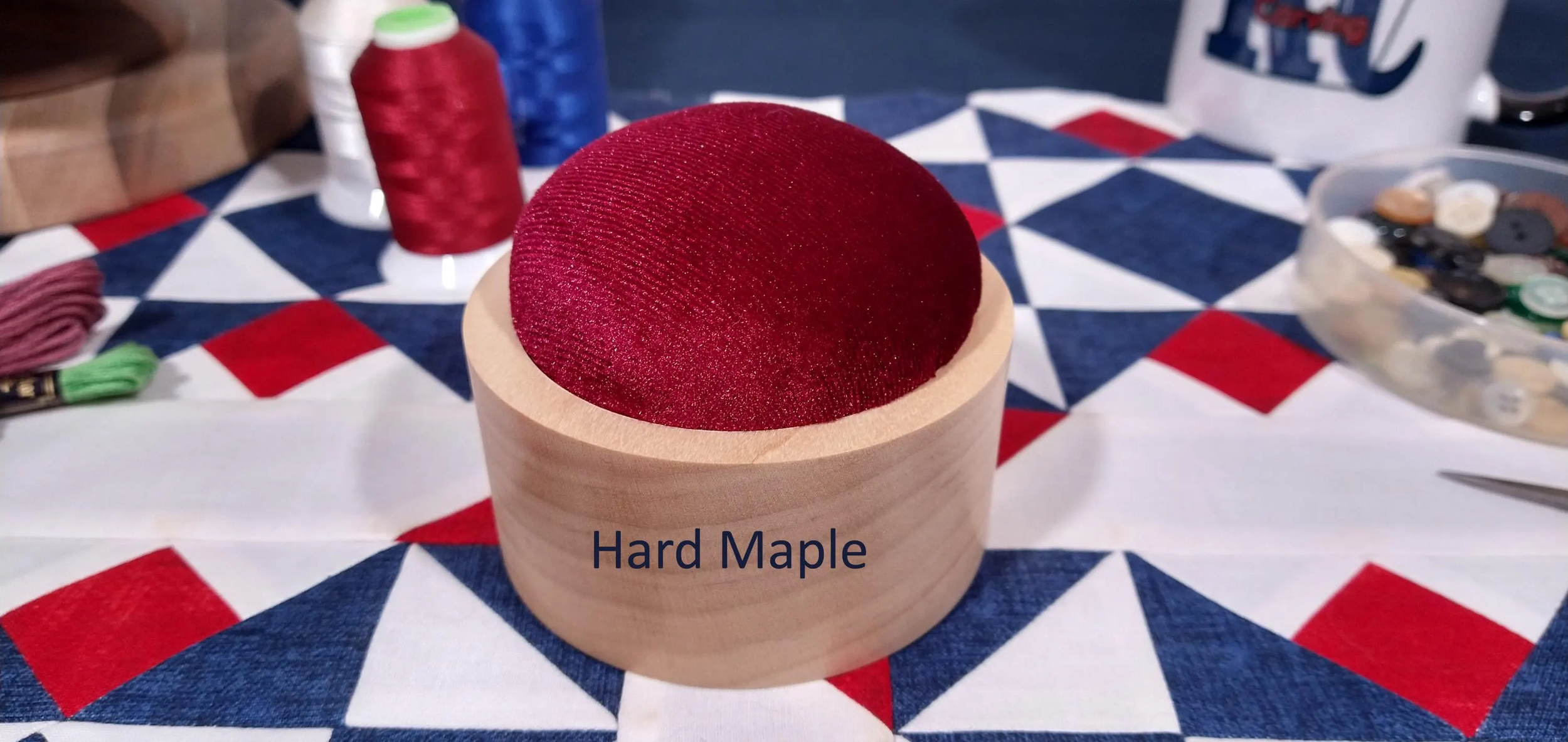 Hard maple handmade pin cushion with burgundy velvet material displayed on a red, white, and blue, quilt block.
