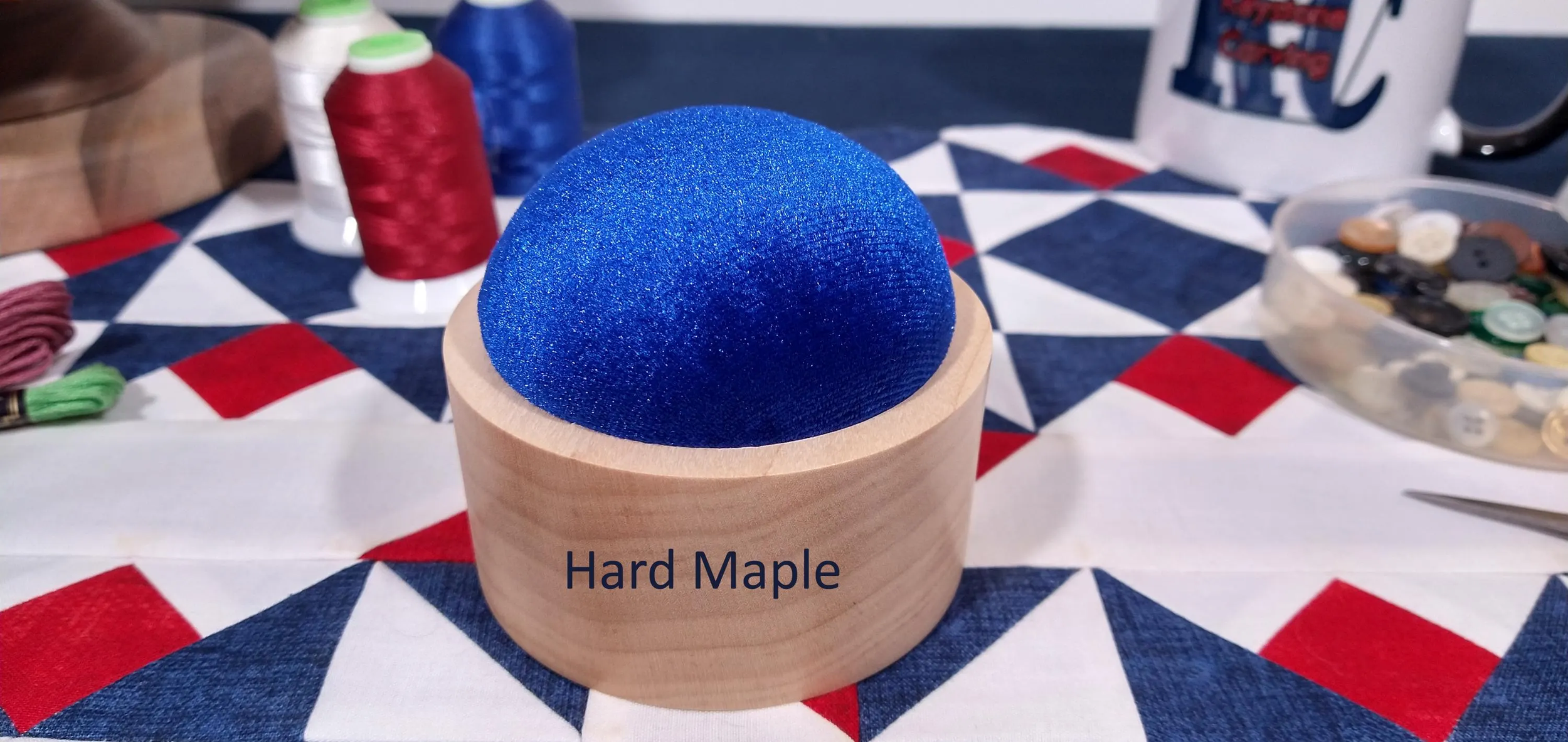 Hard maple handmade pin cushion with royal blue velvet material displayed on a red, white, and blue, quilt block.