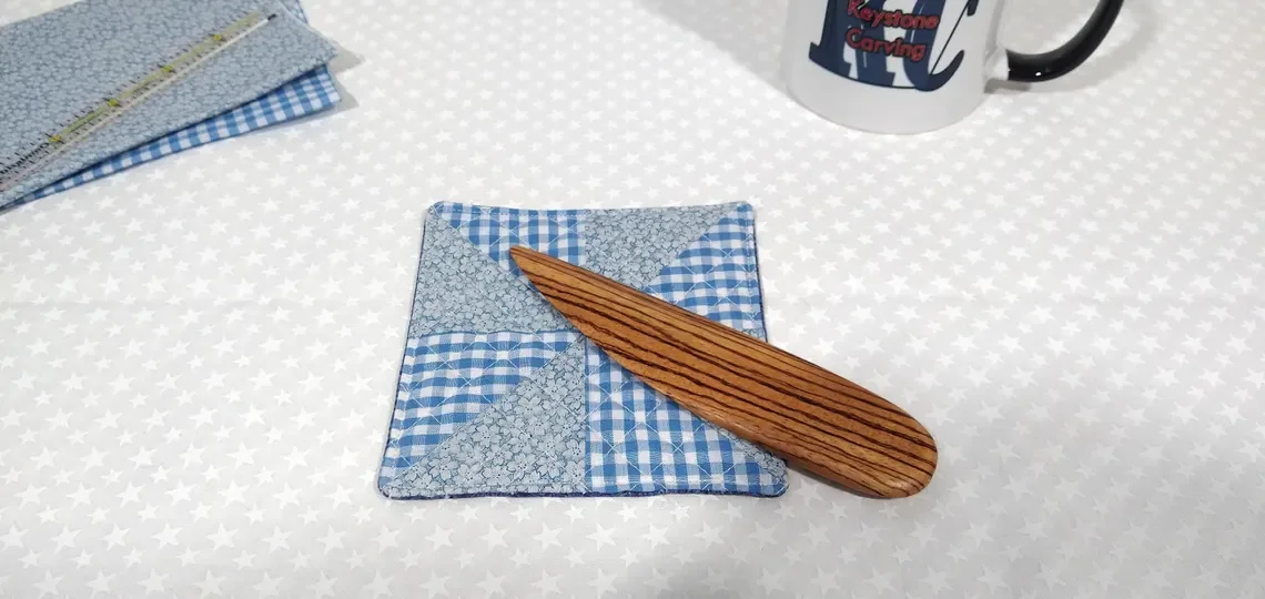 Display of a handmade zebra wood point turner laying on a blue and white checkered pillow