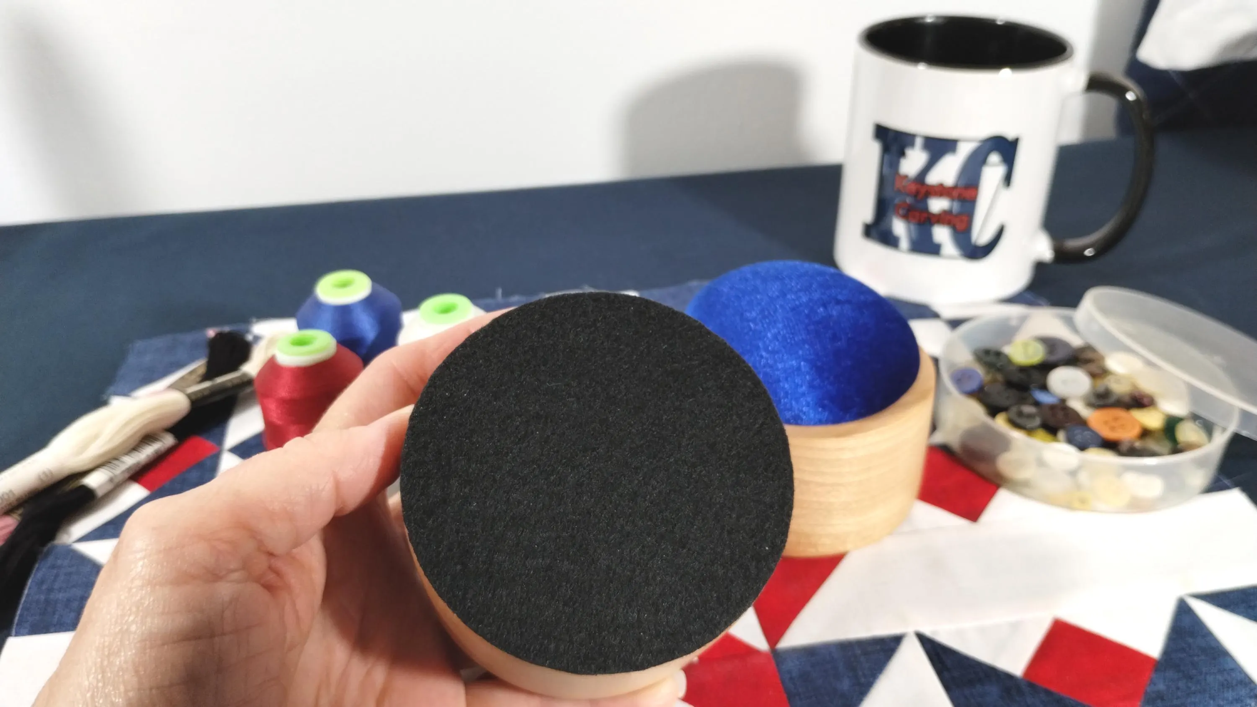 Pincushion held in a delicate hand to show the black felt bottom of the handcrafted pin cushion