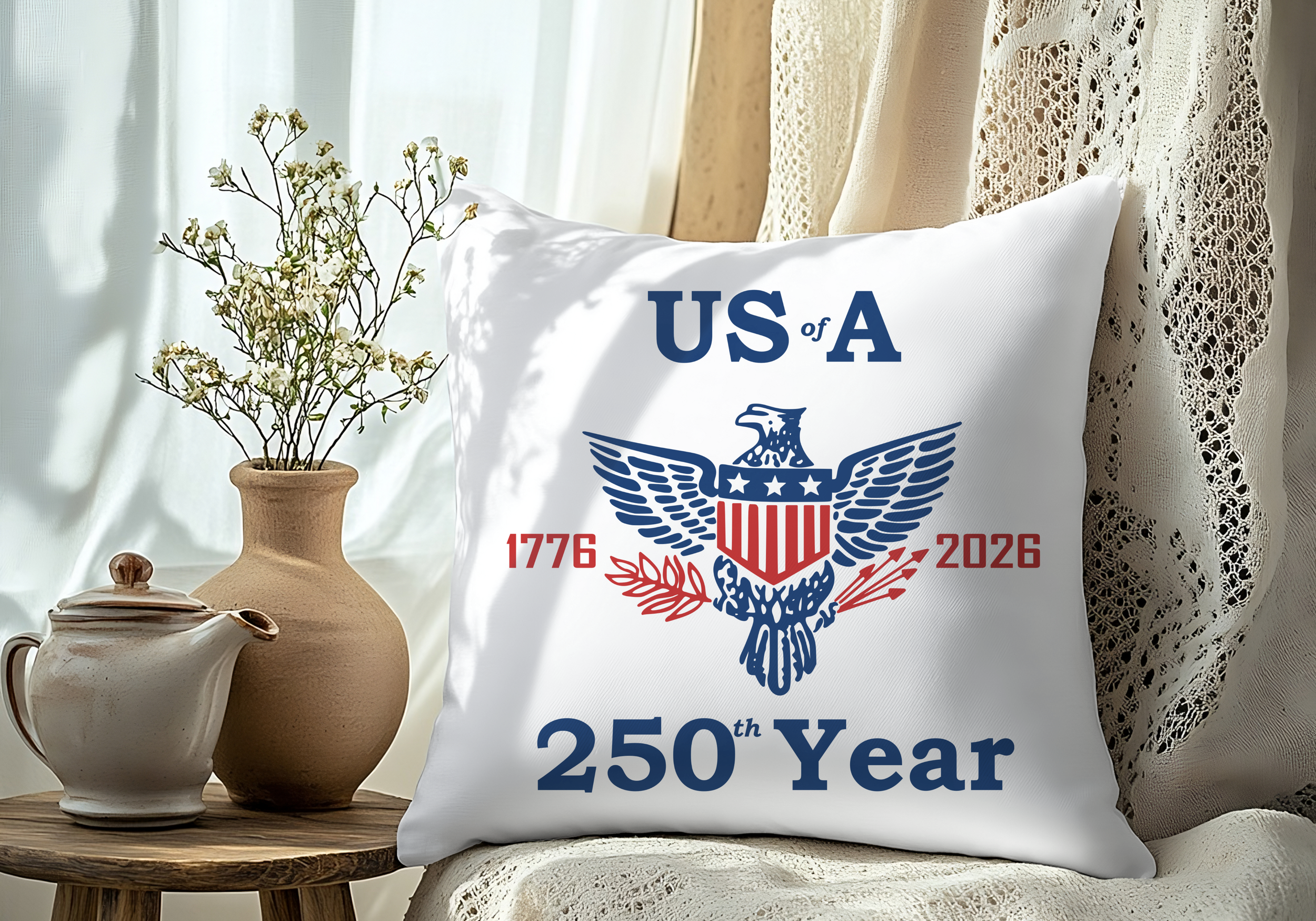 Showing a square white interior pillow with a retro American eagle and red and blue text reading US of A 1776 2026 250th Year. The pillow is shown sitting on a chair up against a laced curtain.
