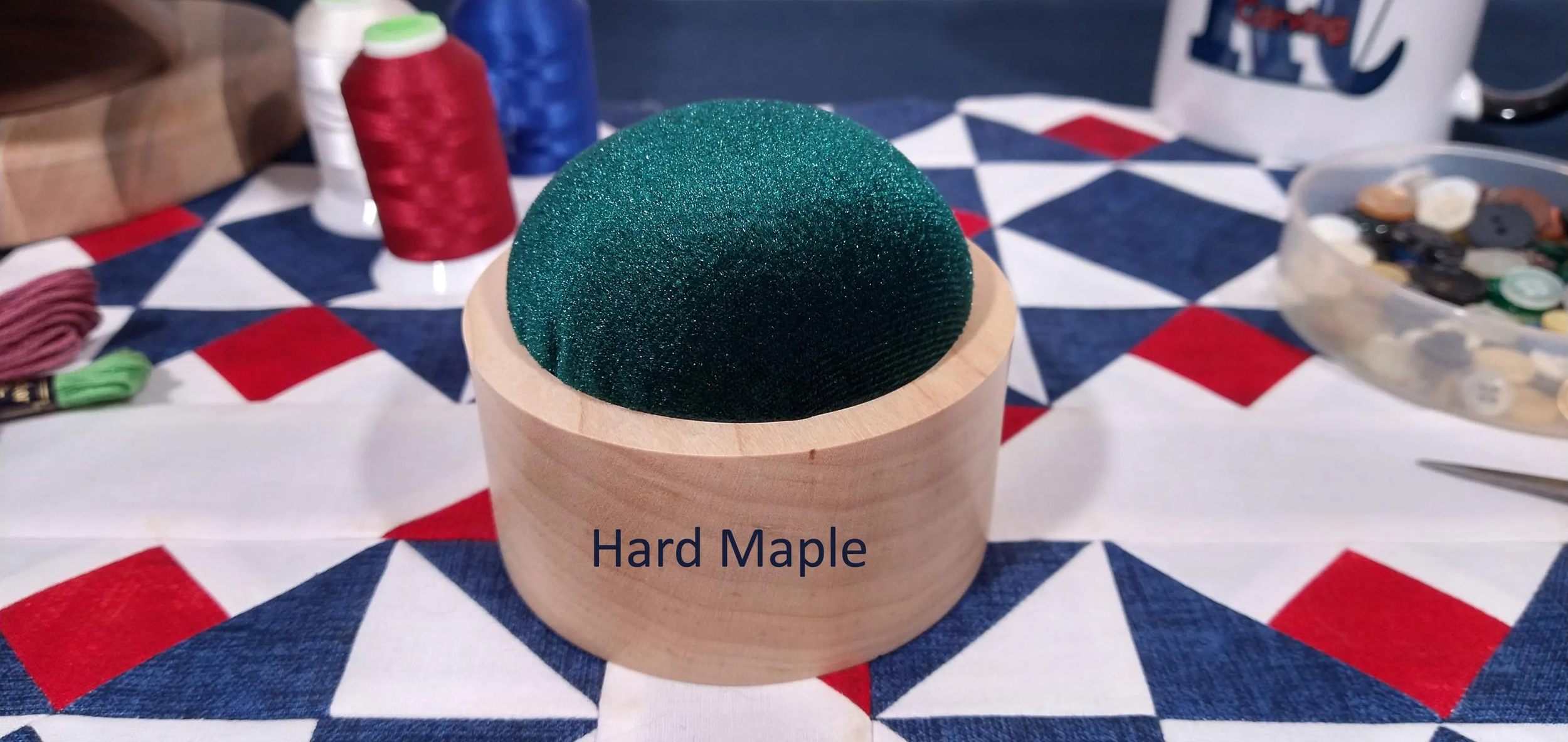 Hard maple handmade pin cushion with hunter green velvet material displayed on a red, white, and blue, quilt block.