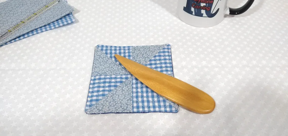 Display of a handmade yellow heart point turner laying on a blue and white checkered pillow