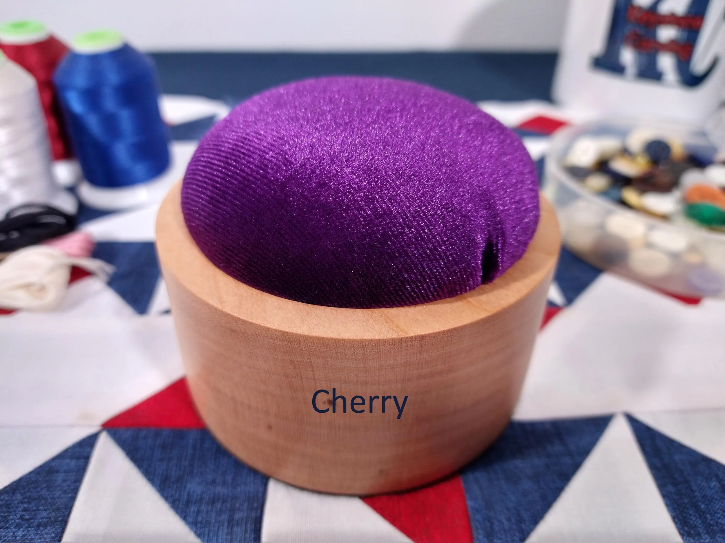 Zoomed in front side of a cherry wood pincushion with purple velvet fabric