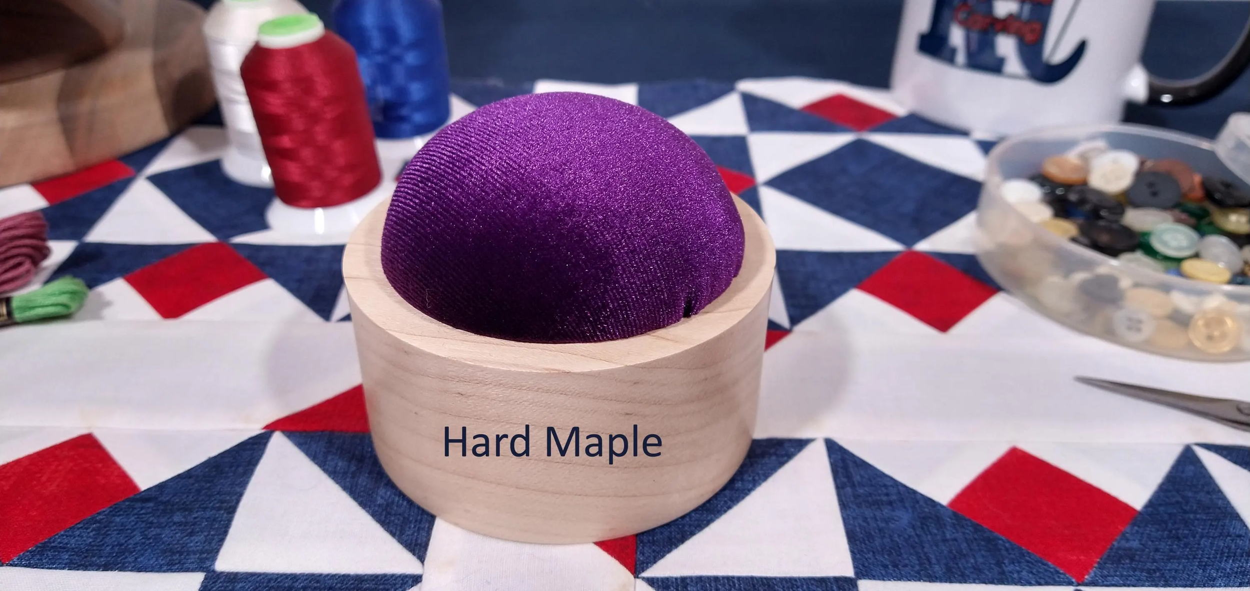 Hard maple handmade pin cushion with purple velvet material displayed on a red, white, and blue, quilt block.
