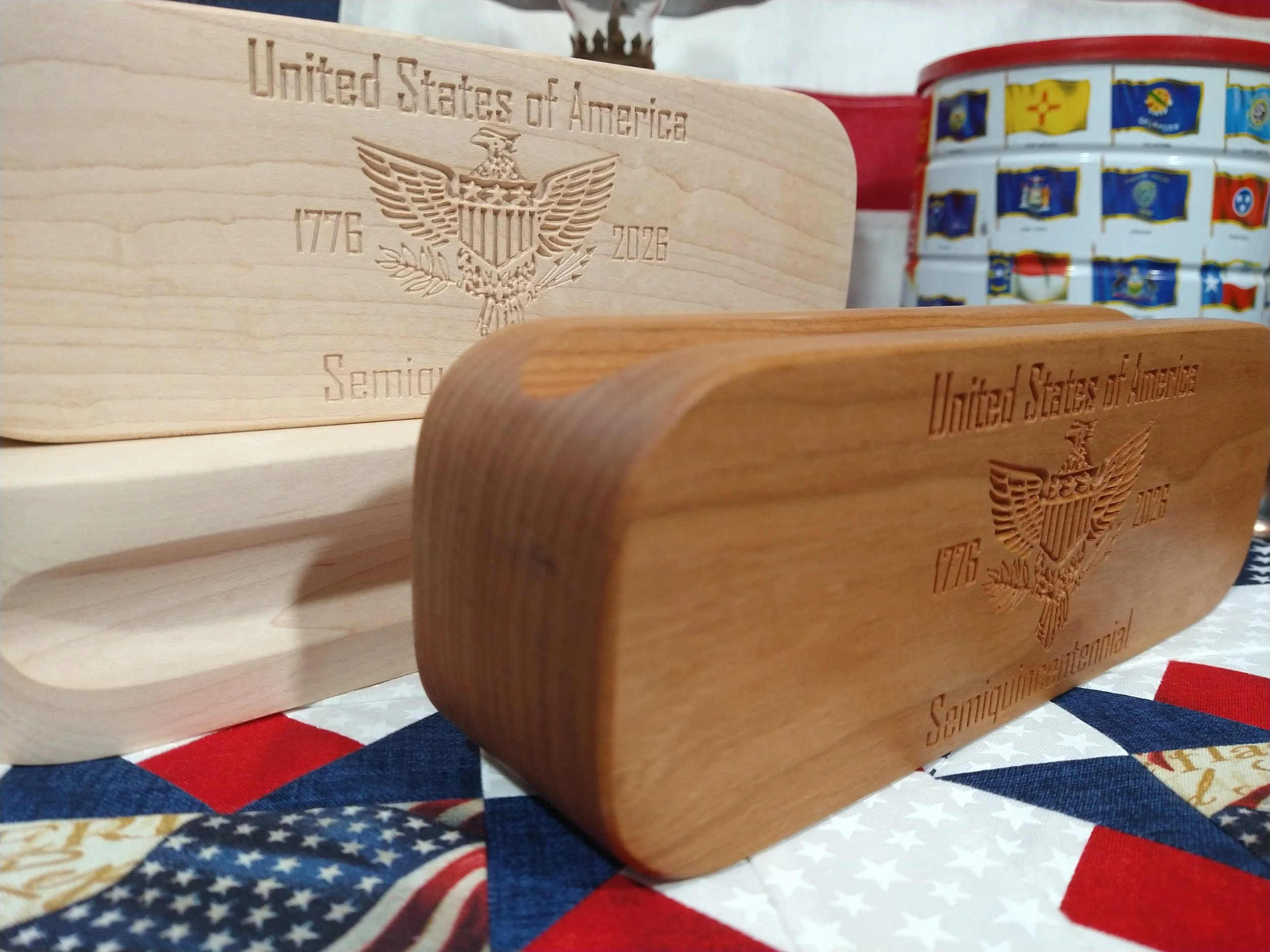 Side view of a hard maple and a cherry wood clapper carved with The United States of America Semiquincentennial