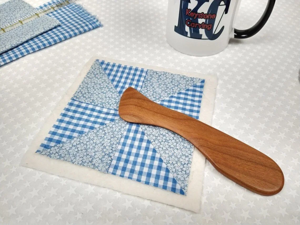 Display of a handmade cherry Hera marker laying on a blue and white checkered quit block