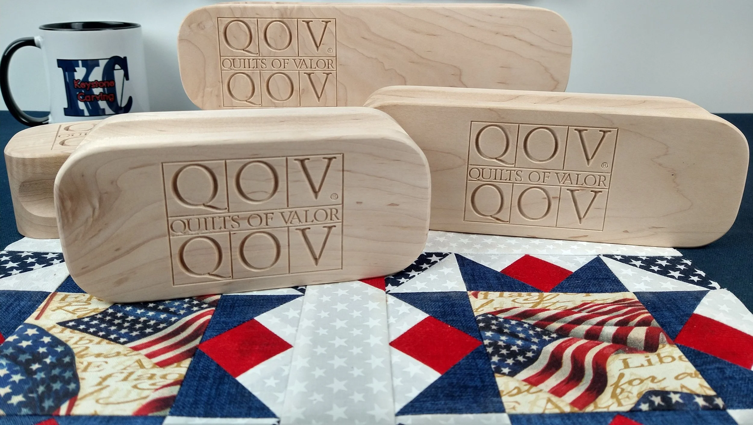 Quilters Clapper wood carved with 'Quilts of Valor QOV,' a patchwork quilt with American flag pattern, and a 'Keystone Carving LLC
