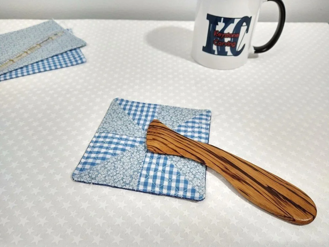 Display of a handmade zebra wood Hera marker laying on a blue and white checkered quit block