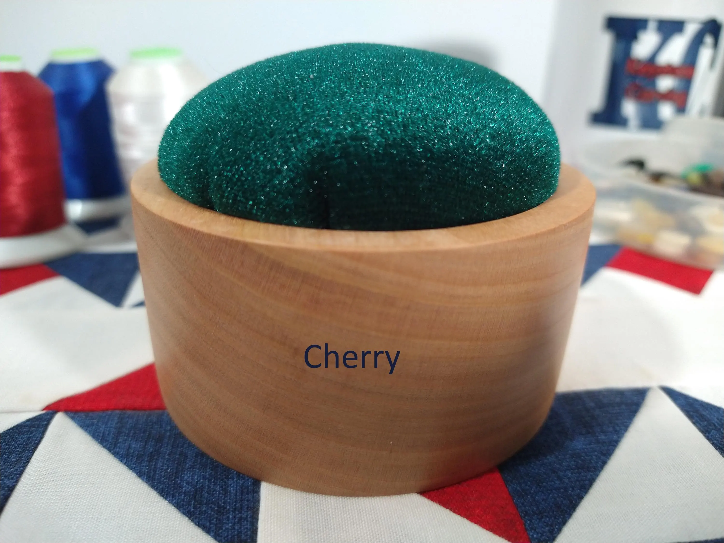 Zoomed in front side of a cherry wood pincushion with royal green velvet fabric