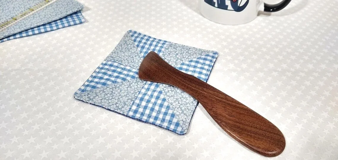 Display of a handmade walnut Hera marker laying on a blue and white checkered quit block