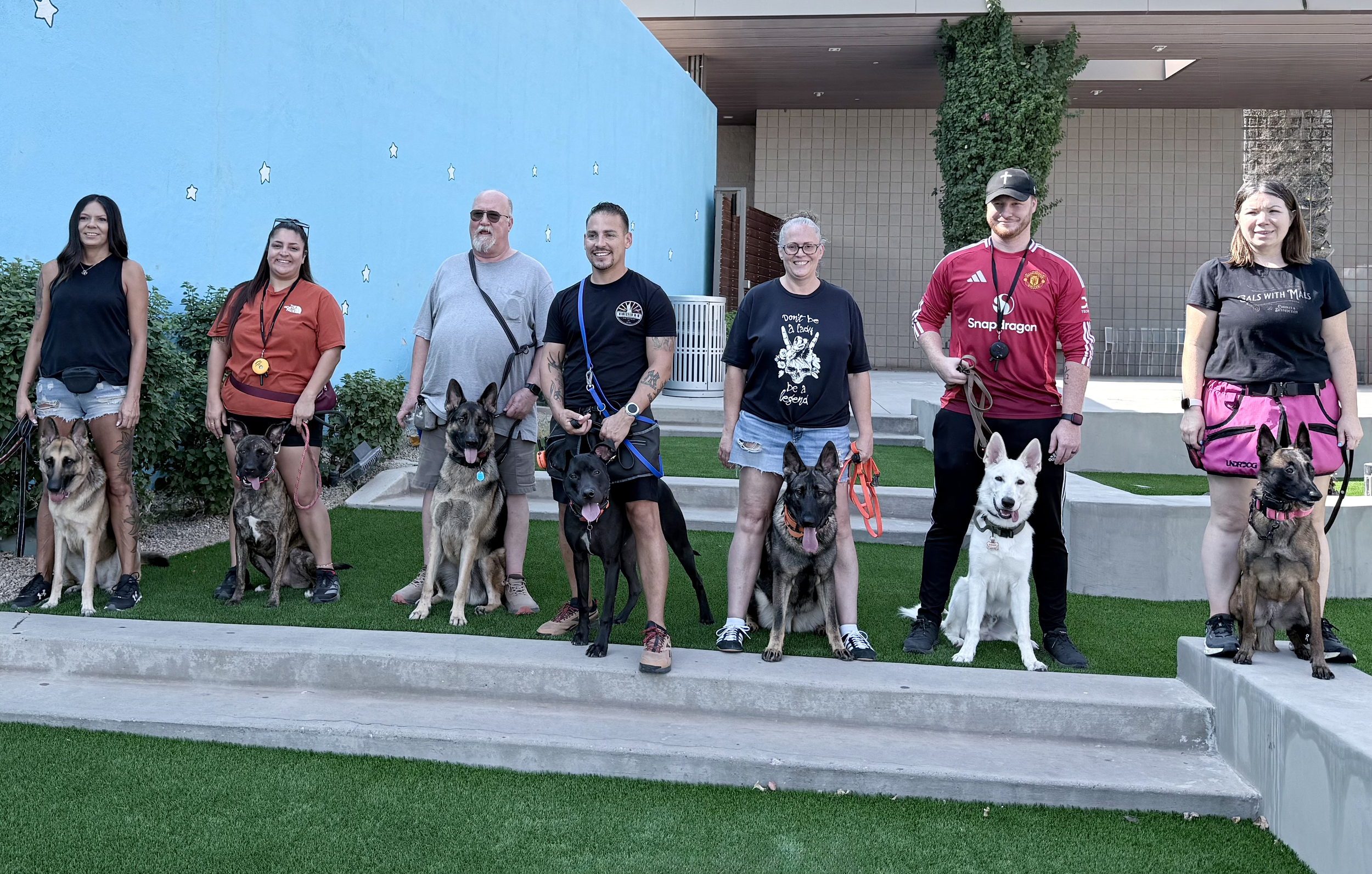 Go with Option 1:  A group of dog owners and trainer posing with their trained dogs during a Kinected K-9 session in Surprise, Arizona.