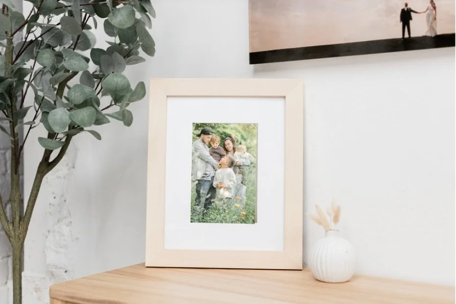 Ein Familienfoto in einem weißen Rahmen auf einem Holztablett. Es zeigt fünf Menschen im Grünen, vermutlich Familie, die schöne Momente teilen.