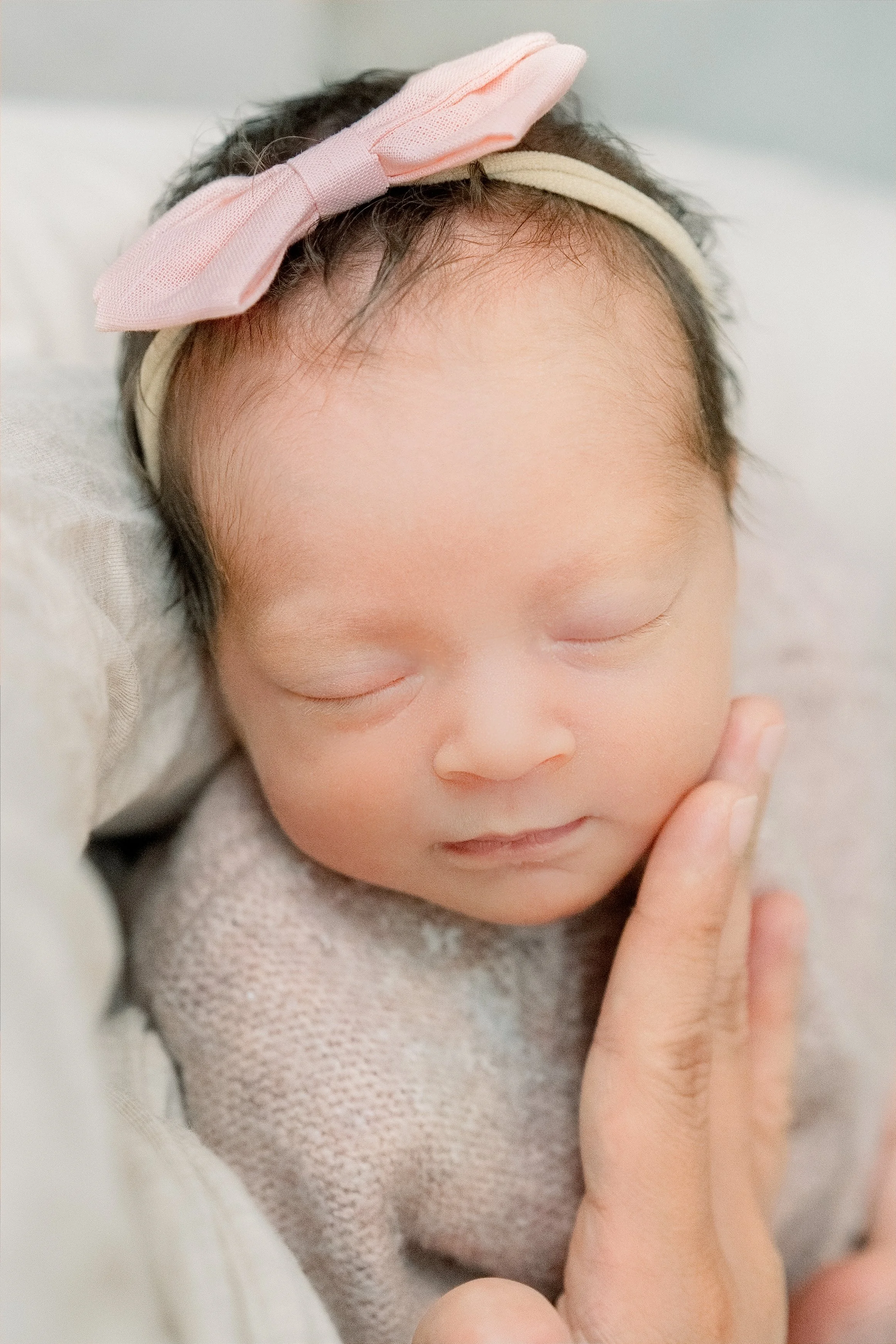 Ein schlafendes Baby, das in einem weißen Handtuch eingewickelt ist, liegt auf einem Hautfarbenen Stoff und hat einen kleinen Lavendelzweig neben sich.
