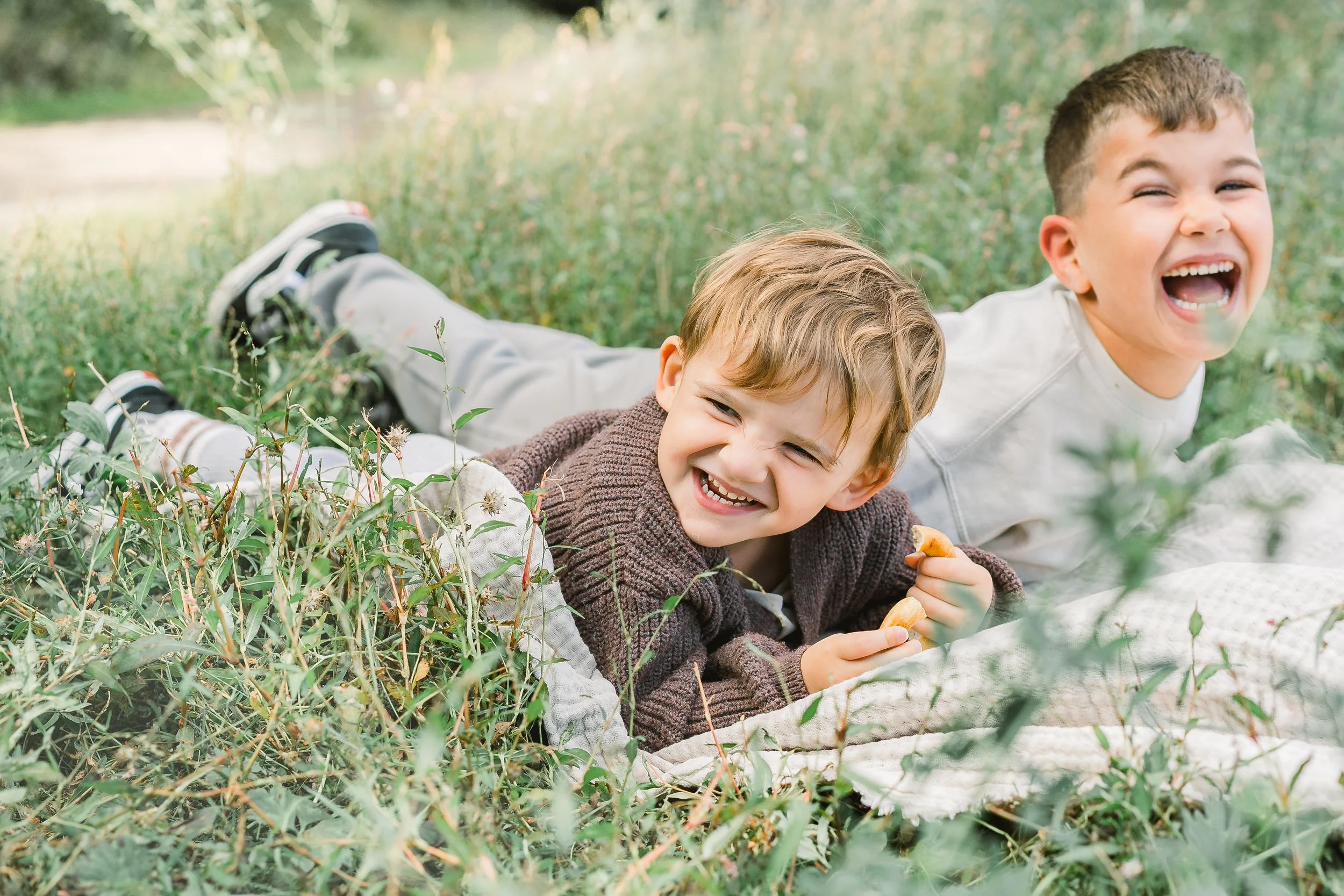 Zwei lachende Jungen liegen im Gras und essen Kekse.