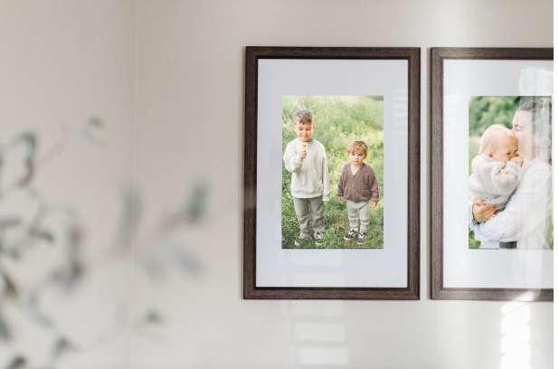 Zwei eingerahmte Familienfotos an einer Wand. Das erste zeigt zwei Jungen im Freien, das zweite ein Baby beim Kuscheln mit einer Frau.