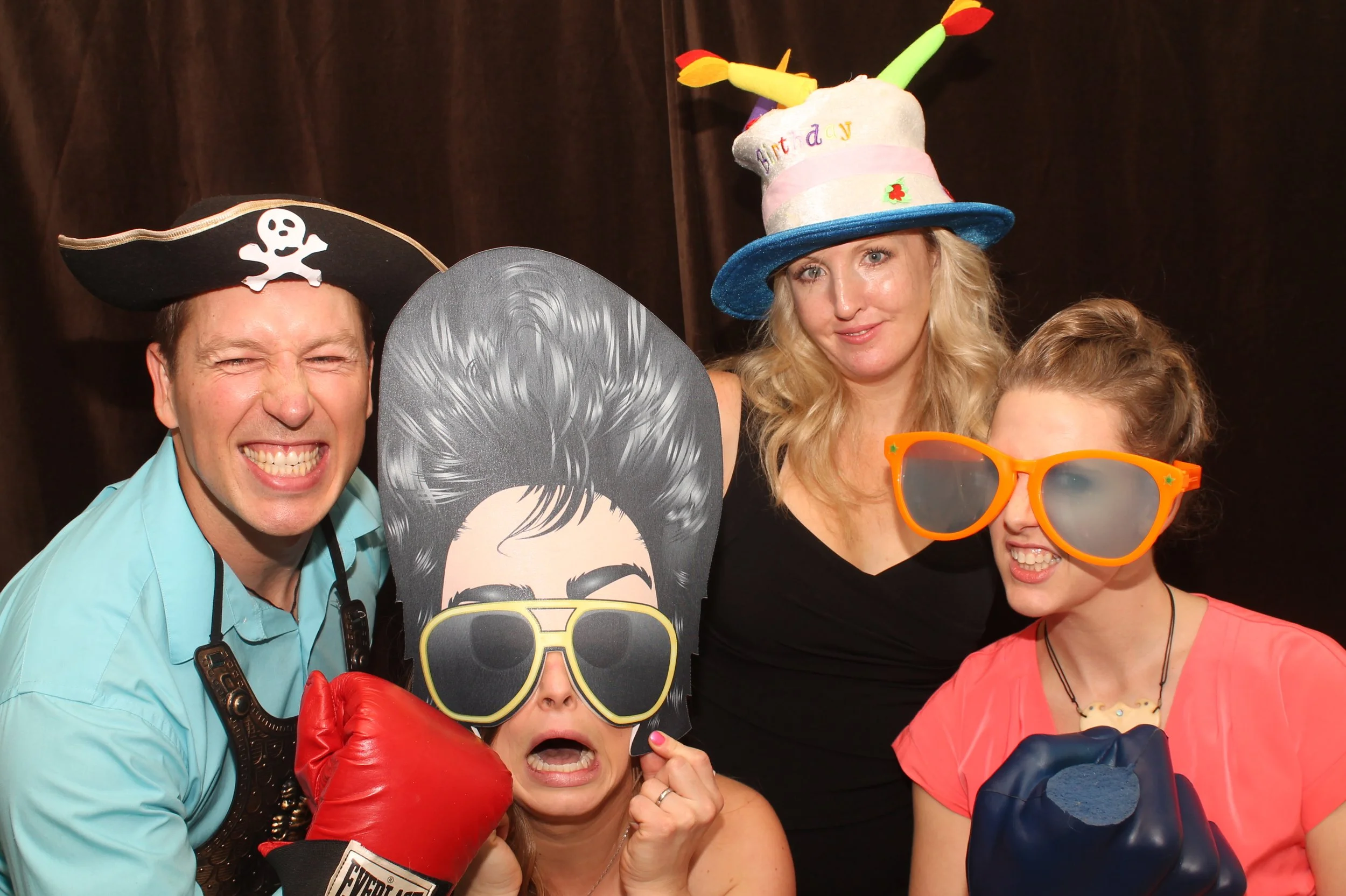  Four people in fun hats and oversized glasses, one with boxing gloves, are joyfully posing in a Vancouver mirror photo booth. Their laughter echoes the excitement that Vancouver photo booth rental services bring to every event. 