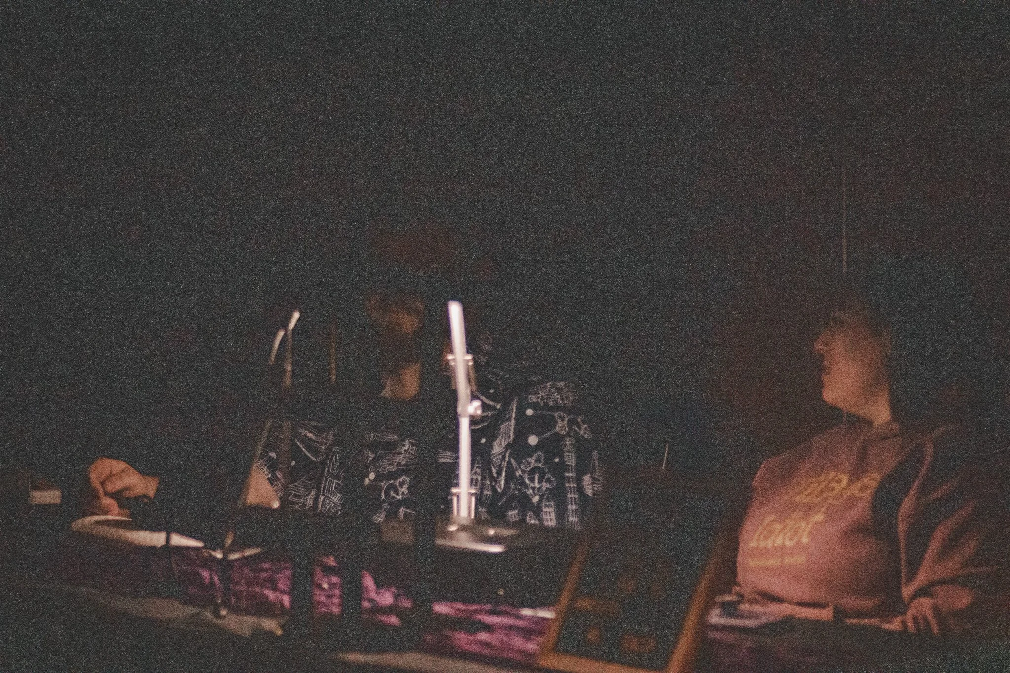 Two people sitting at a table in a dimly lit room, engaged in conversation, with a microphone and a picture frame on the table.