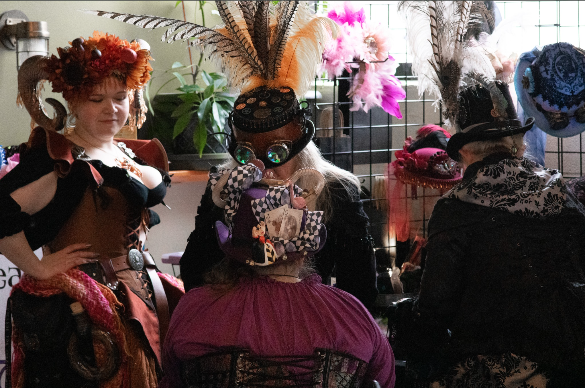 Group of people in steampunk costumes with elaborate hats and accessories at a market stall.