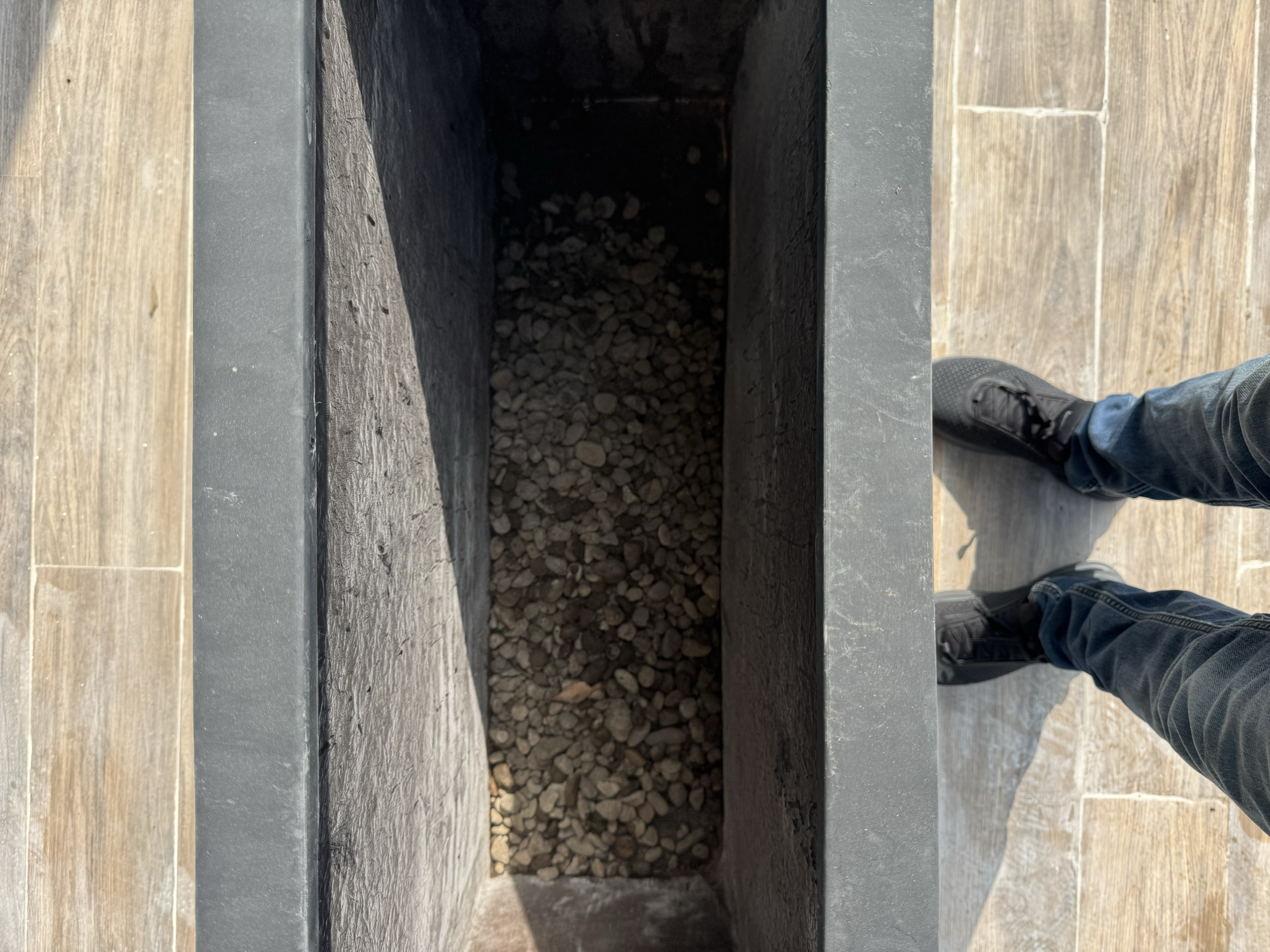 Vista desde arriba de un horno de leña vacío con fondo de ladrillos y dos personas con pantalones y zapatos oscuros a los lados.