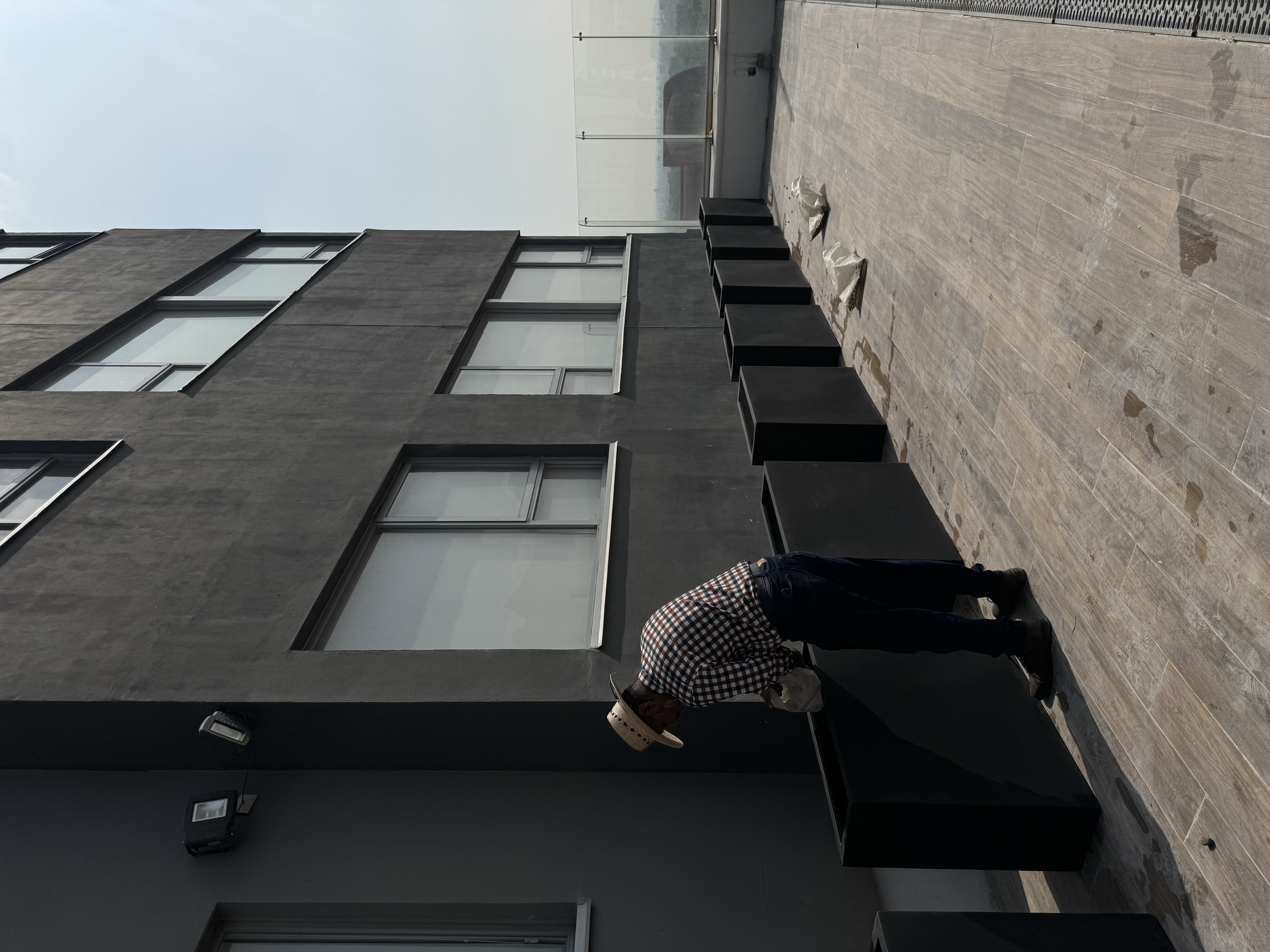 Persona inspeccionando mobiliario en una terraza de edificio moderno de color gris oscuro.