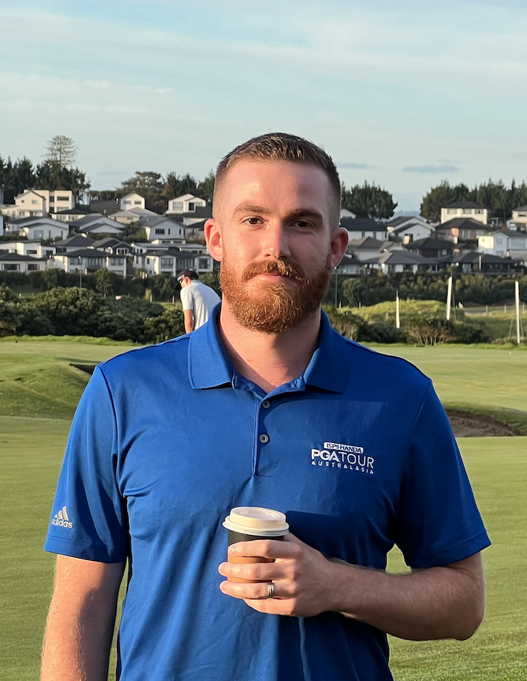Leon Lindsay-Russell, Physiotherapist, wearing a blue PGA Tour Australasia shirt holding a coffee cup on a golf course with houses in the background.