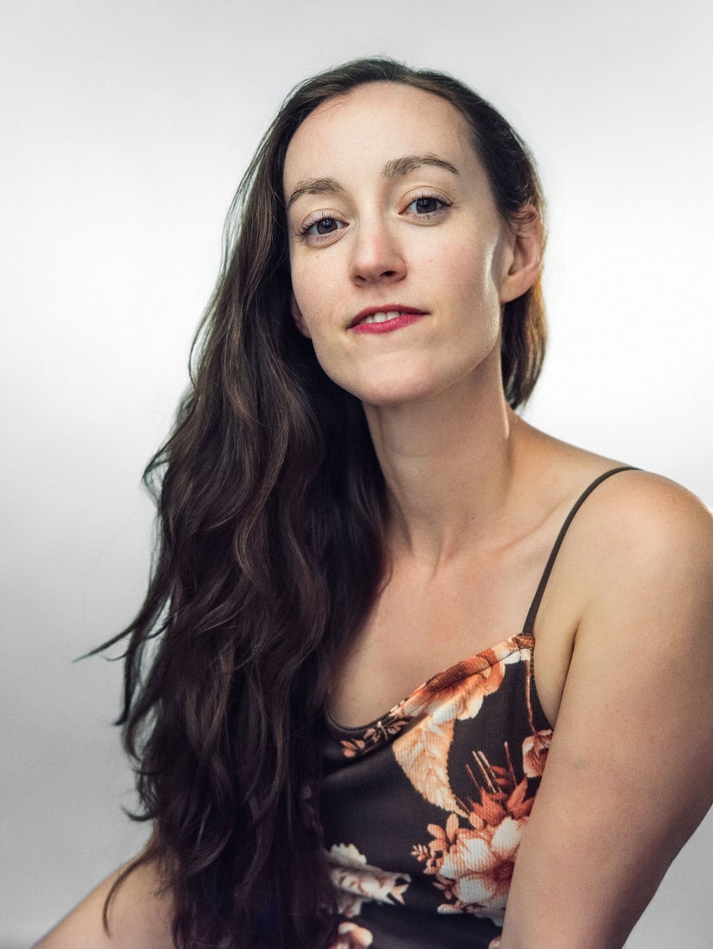Close-up of a woman with long brown hair, smiling, against an orange background.