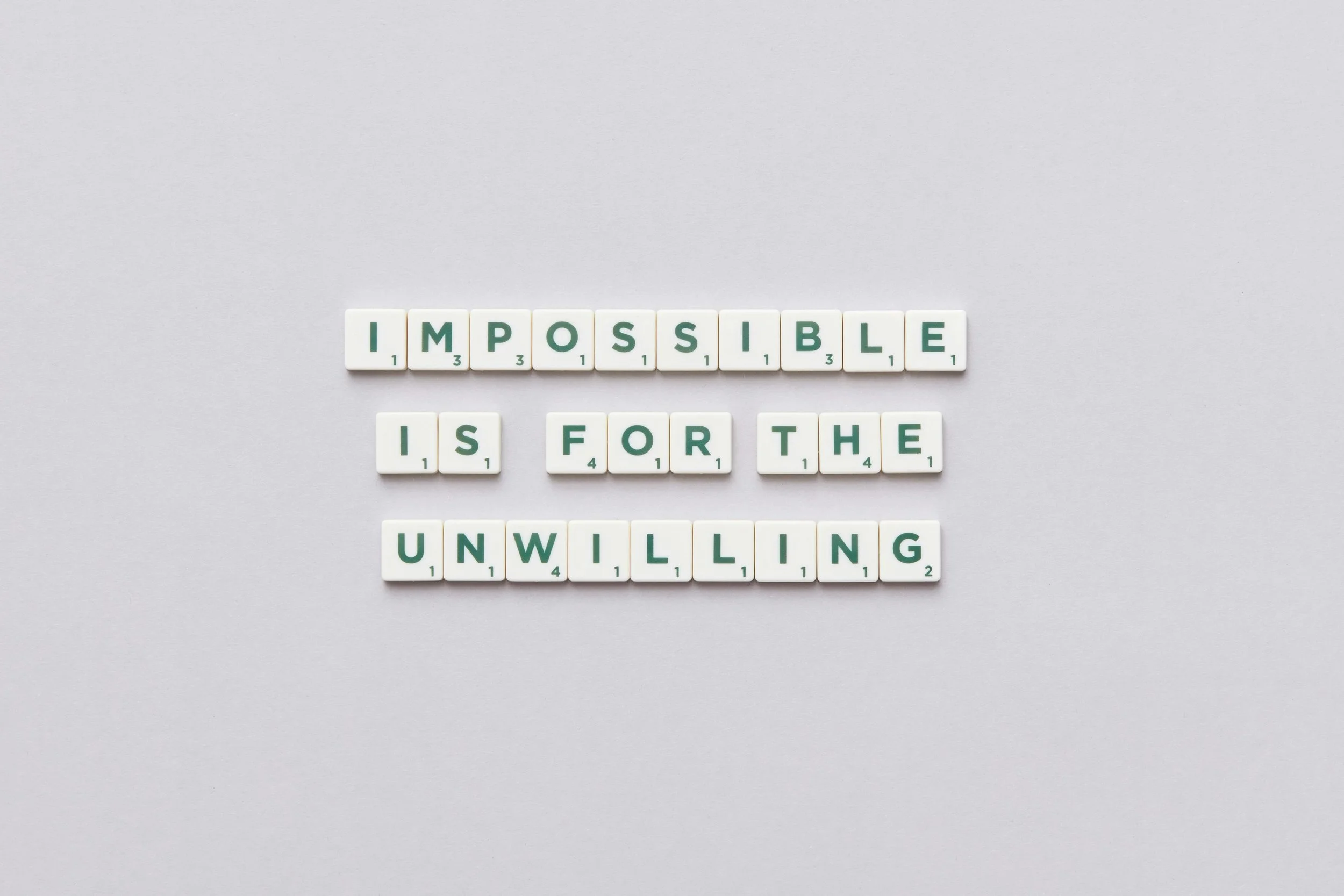 Scrabble tiles spelling out "impossible is for the unwilling".
