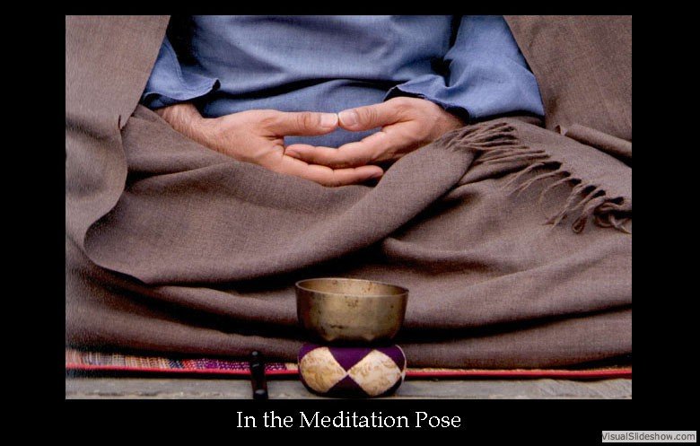 Person sitting cross-legged in meditation pose with hands resting on lap, wearing loose clothing, with a singing bowl and cushion in front.