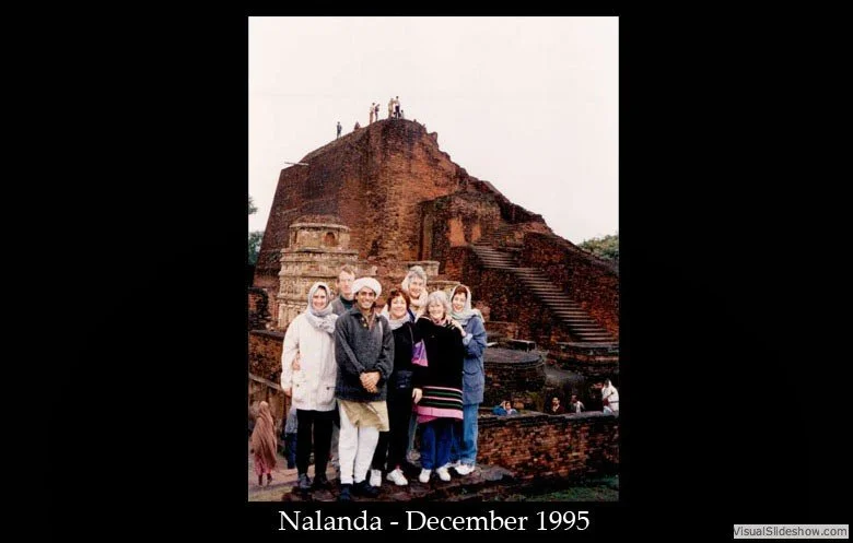 A group of tourists standing in front of an ancient brick monument with stairs and people on top, taken in December 1995 in Nalanda.