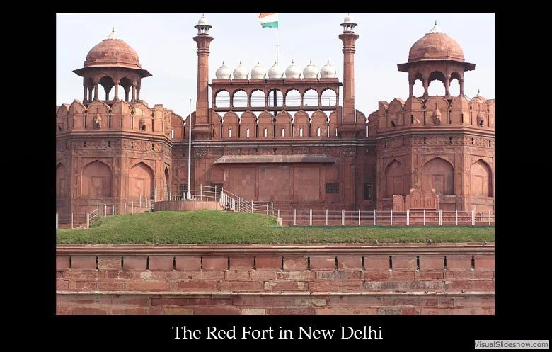 The Red Fort in New Delhi, India, built with red sandstone, featuring domed towers, arches, and a central courtyard, with a flag flying on a flagpole.