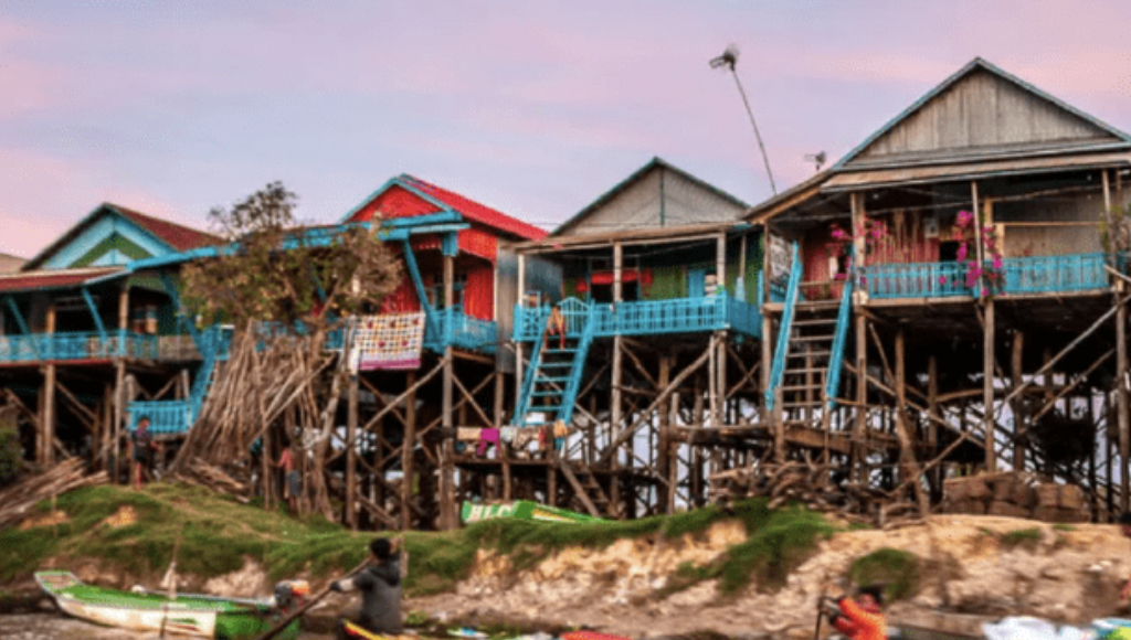 Close-up of a historic red sandstone fortress with rounded towers and battlements, entrance gate in the center, against a partly cloudy blue sky.