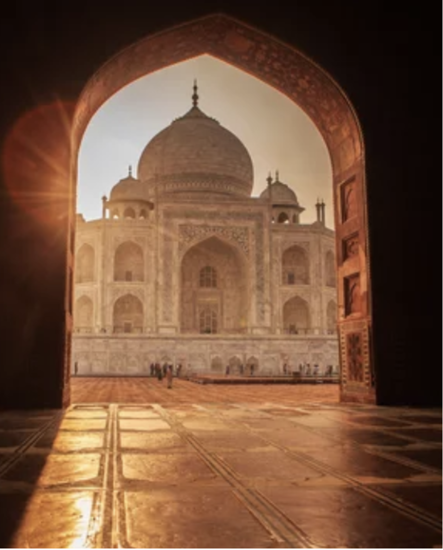 The Taj Mahal seen through an open doorway at sunset, with warm golden light illuminating the marble monument.