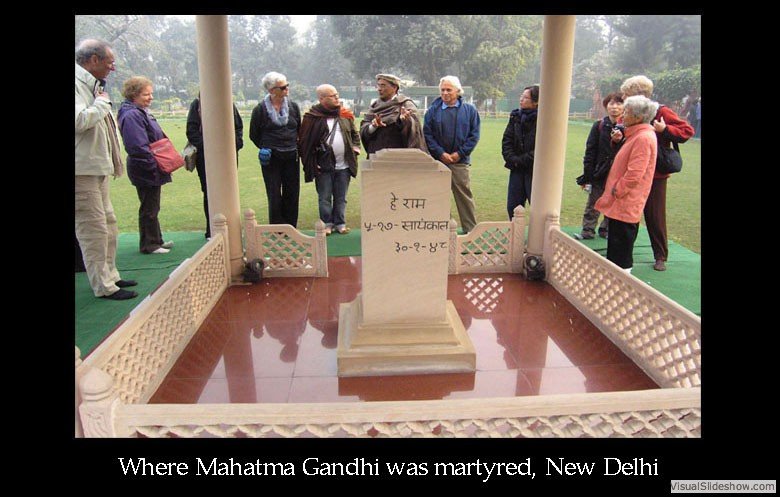 Group of people standing around a memorial shrine for Mahatma Gandhi in New Delhi, with a carved stone plaque and railing, on a misty day.